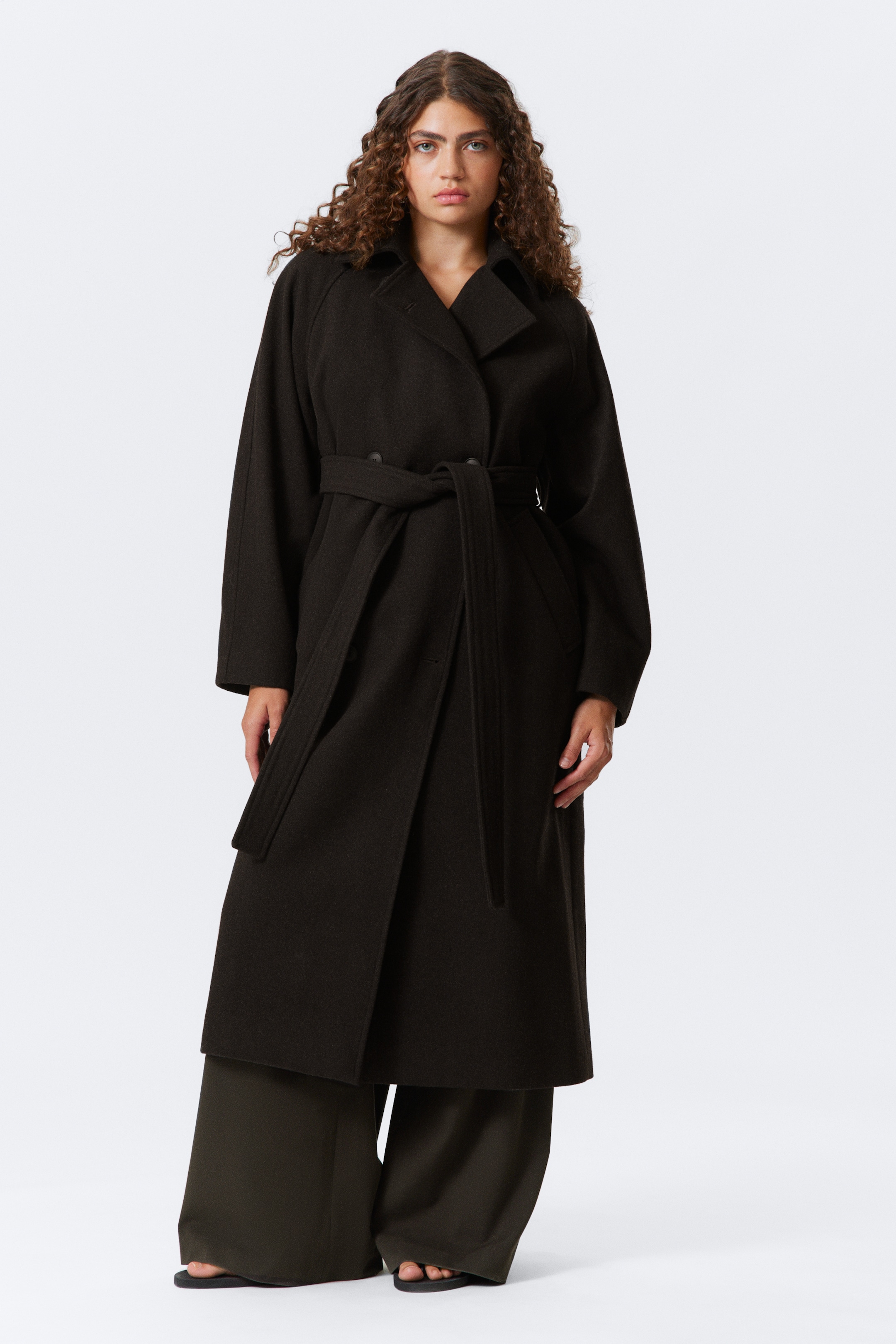 Agrandir l'image: Un manteau long brun foncé est présenté face à l'avant. De larges revers et des manches larges de style dolman façonnent son design, avec une ceinture en tissu assorti nouant le manteau à la taille, créant une silhouette décontractée et surdimensionnée.