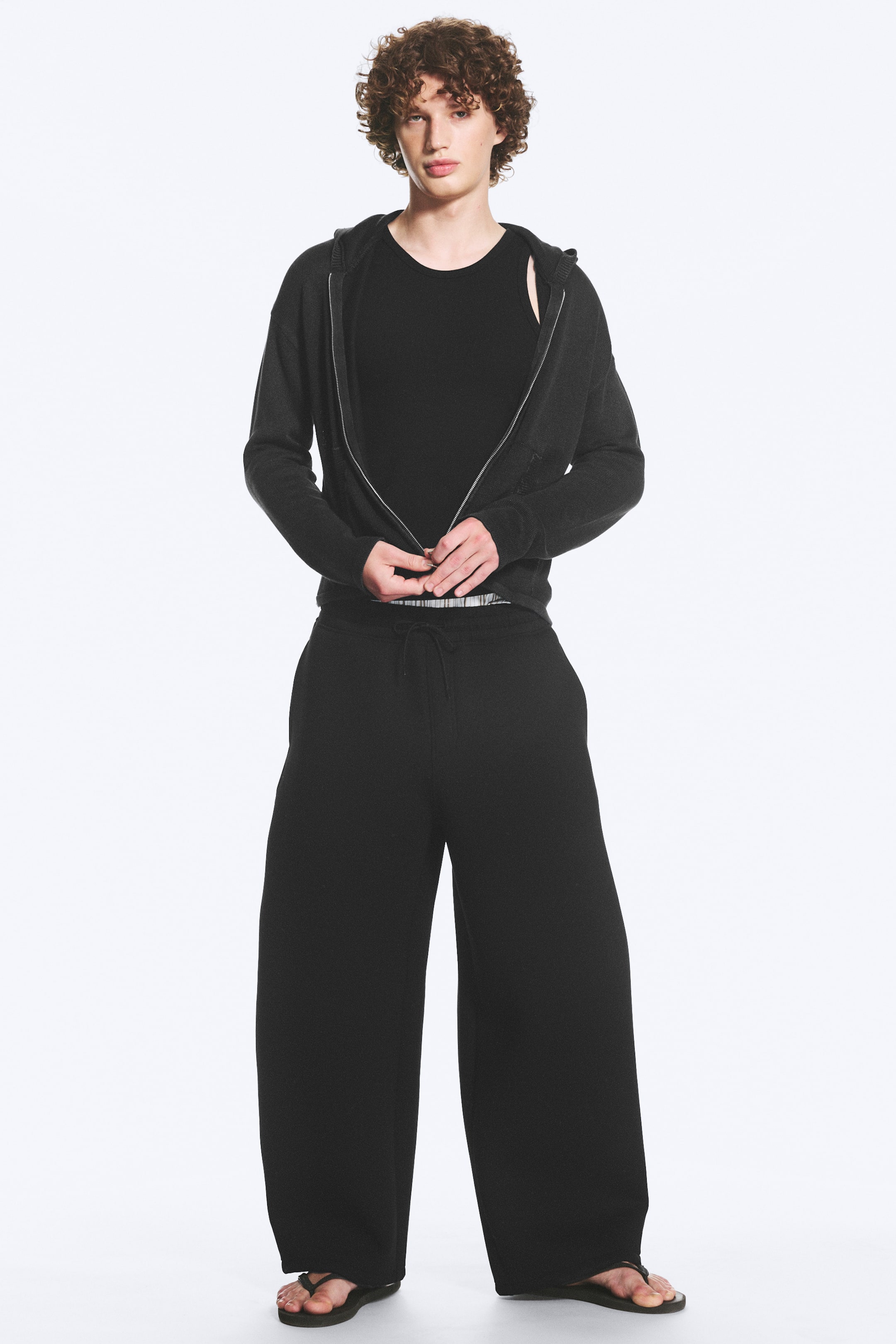 Grotere afbeelding bekijken: Cody scuba joggingbroek is zwart, heeft wijde pijpen en wordt gedragen door het model. Ze zijn gemaakt van een gladde, gestructureerde stof, hebben een elastische tailleband met trekkoord en zijzakken.