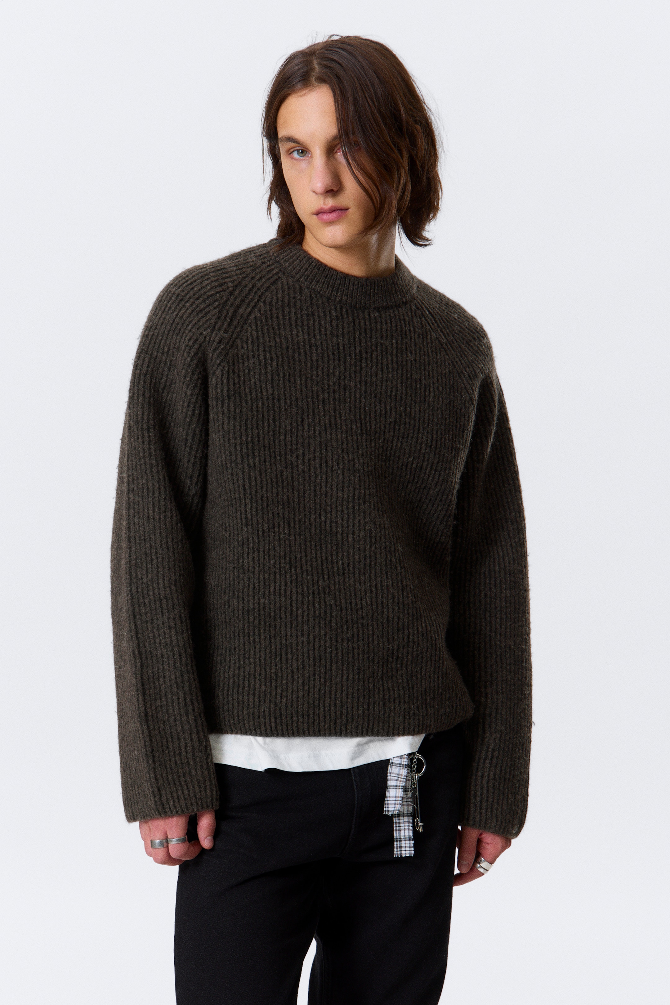 Visa större bild: En mörkgrön, ribbstickad tröja presenteras, med en rund hals, raglanärmar och grova vertikala ribbor överallt. Den bärs med en oversized passform, och en vit t-shirt syns under dess korta fåll.
