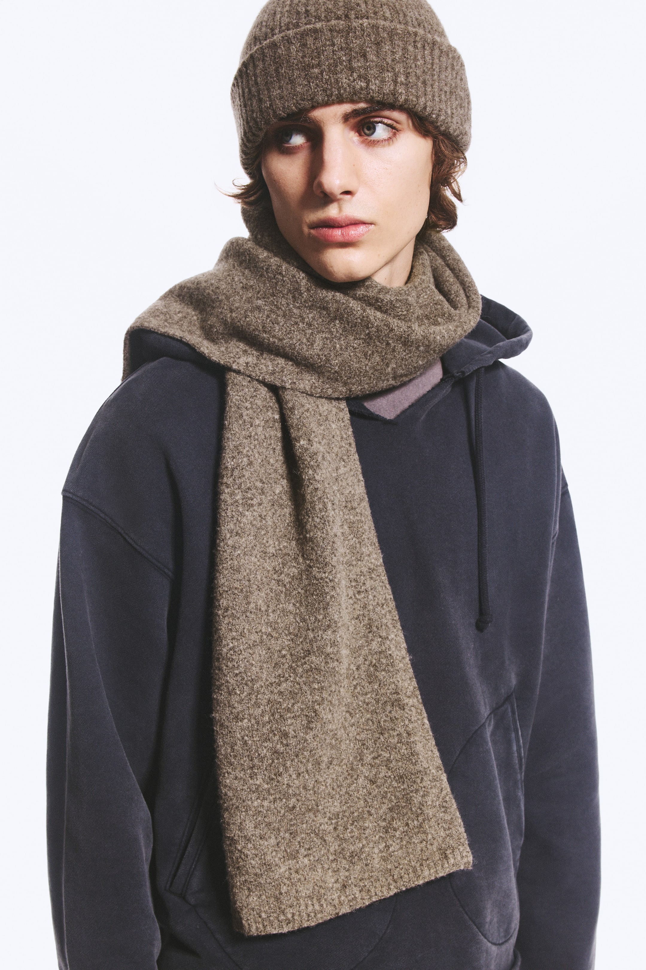 View larger image: A brown, textured wool-blend knit scarf is being worn by the model, wrapped once around the neck with one end hanging down the front. The scarf is styled with a matching brown knit beanie and a dark grey hooded sweatshirt.
