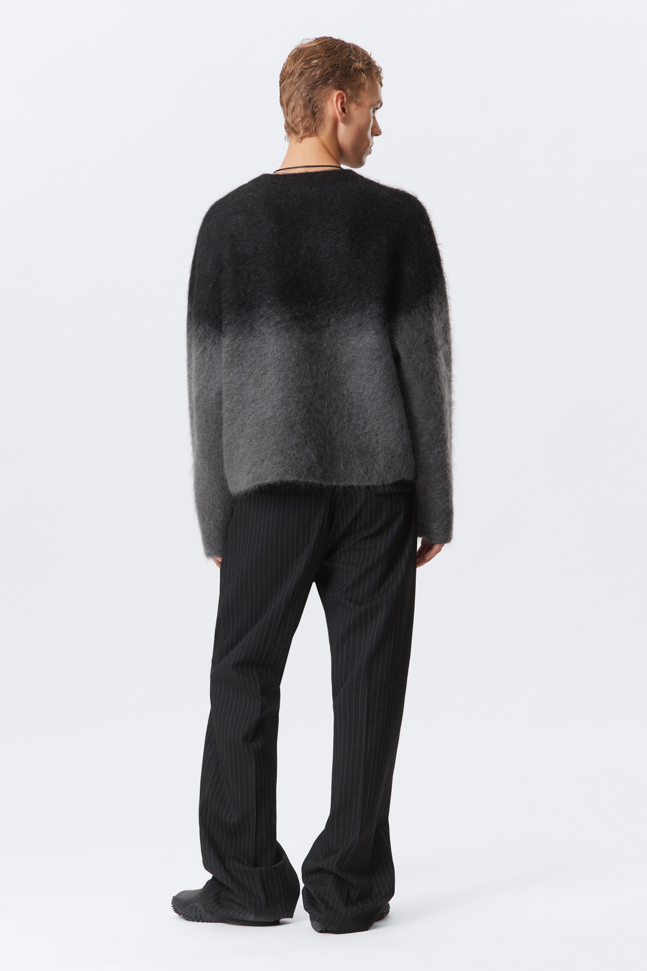 Visa större bild: En tröja med rund hals, lös passform, borstad fluffig textur och en gradient som går från mörk till ljusgrå bärs av modellen. Tröjan har raka fållar och är stylad med mörka byxor med nålrand.