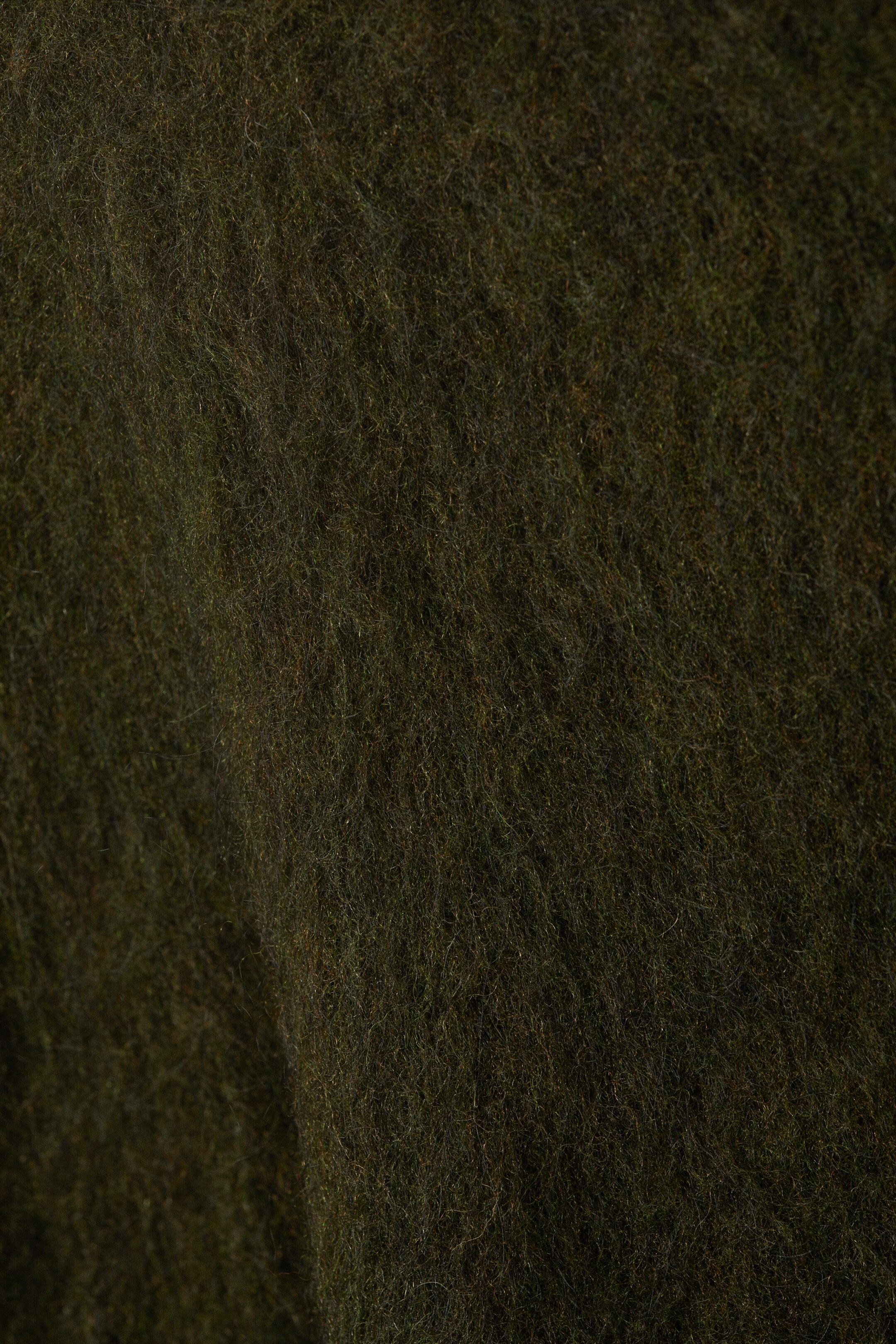 Größeres Bild ansehen: Eine Nahaufnahme zeigt die dunkelgrüne, flauschige Textur eines Mohair-Mischgewebes.