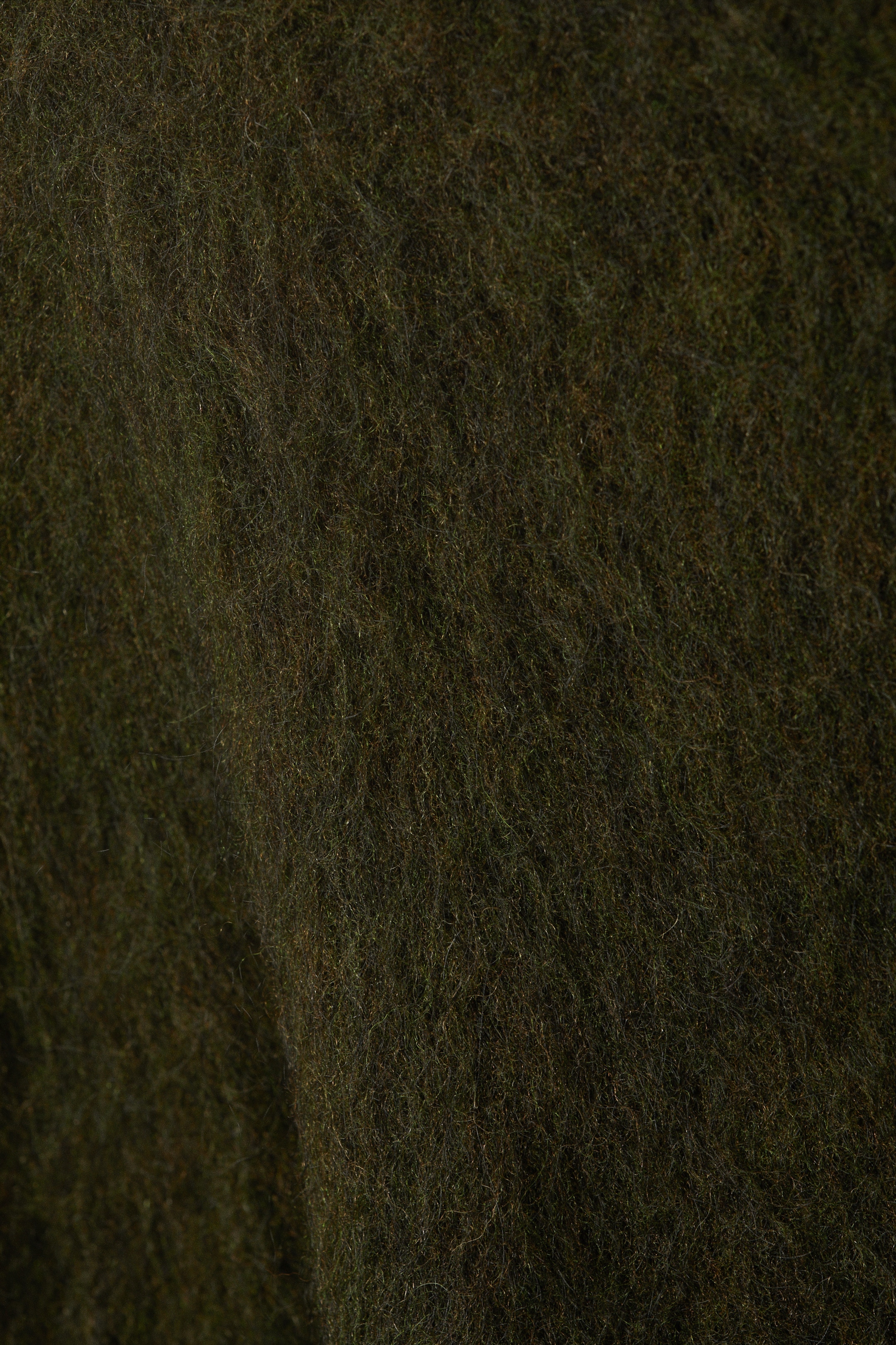 Grotere afbeelding bekijken: Een close-up toont de donkergroene, pluizige textuur van een mohair blend trui.