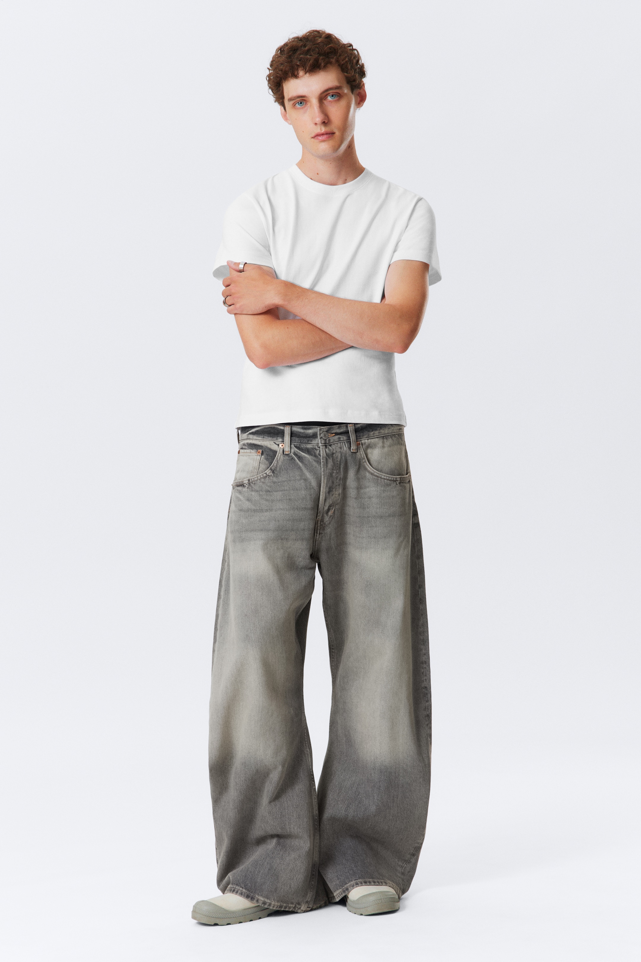 View larger image: A pair of wide-leg, faded grey jeans is being worn by a model, facing forward, showcasing their relaxed fit and visible button fly. The jeans are exhibiting a distinctive washed-out effect, with darker tones appearing at the waistband and lower legs, and lighter areas across the thighs.