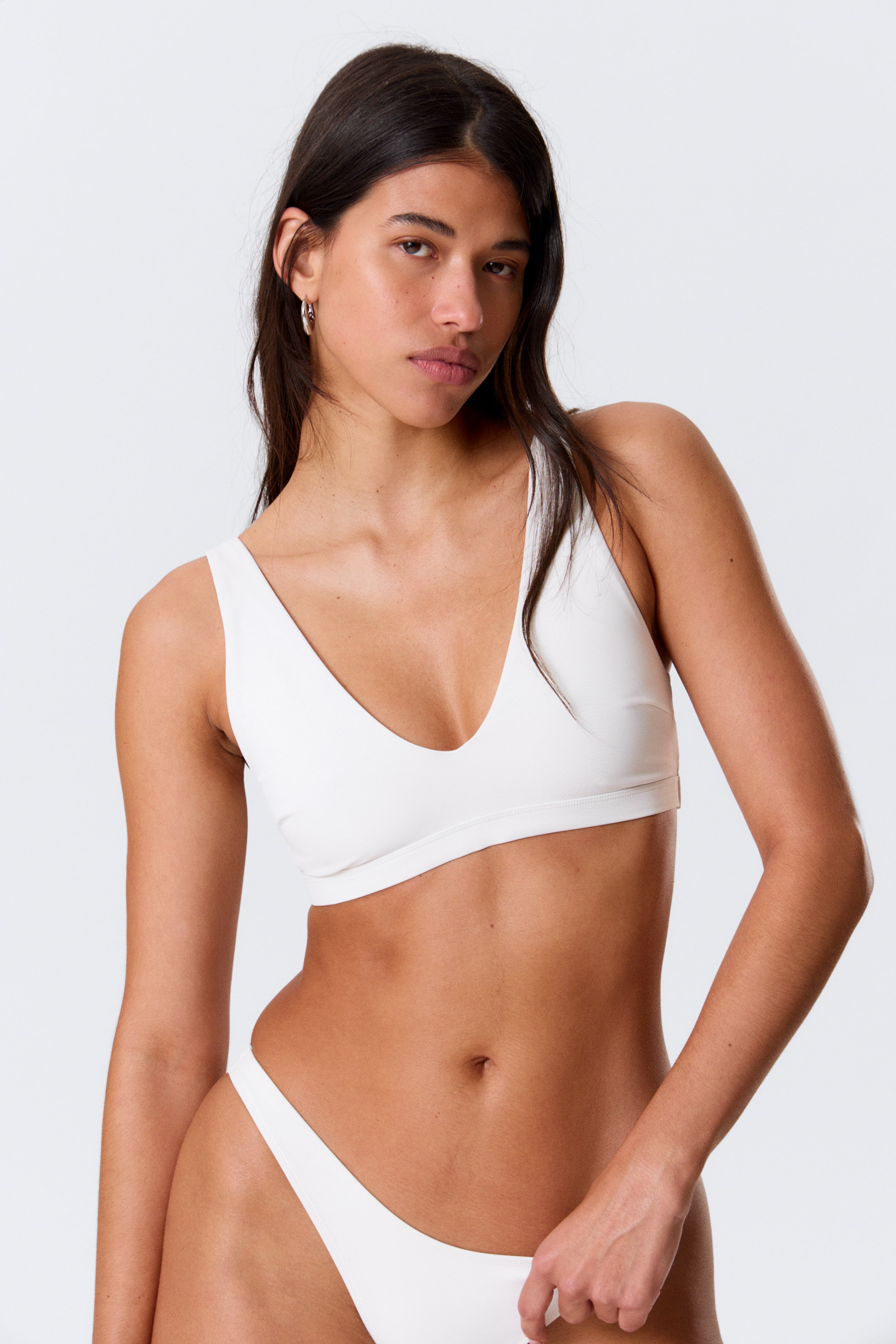 View larger image: A white bikini top featuring a deep V-neckline and wide straps, paired with a matching white high-cut bikini bottom, both presented from a slight front-left angle.