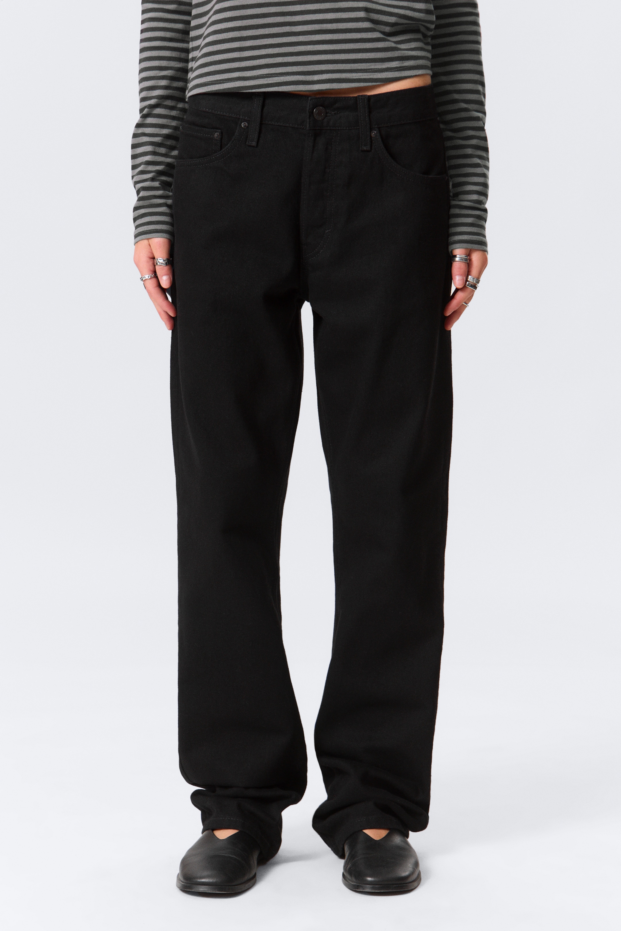 View larger image: Black, relaxed-fit pants are being presented, facing forward. They feature a straight-leg cut and a full length, pooling slightly at the ankles over the wearer's black shoes. Visible details include front pockets and a button closure at the waist.
