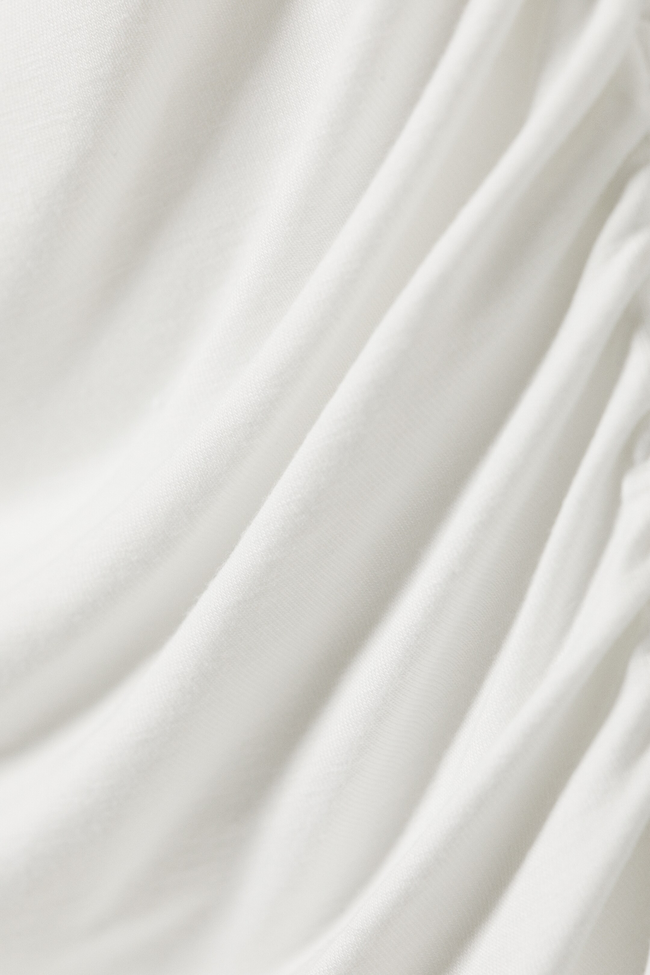 Agrandir l'image: Le tissu blanc présente des plis et des fronces douces. Le matériau montre une texture subtile, avec un ruché plus prononcé sur le côté droit.