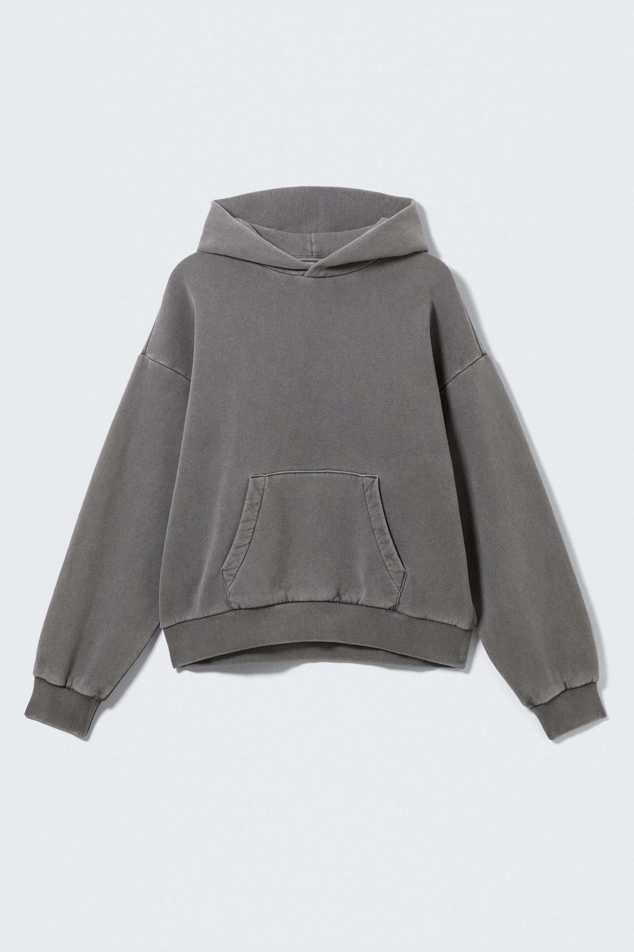 View larger image: A dark grey hoodie is presenting its FRONT, featuring an oversized fit with dropped shoulders, a relaxed hood, and a large kangaroo pocket. It also includes ribbed cuffs and a ribbed hem, all showcasing a stone-washed finish.