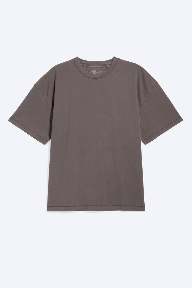 Oversize'owy T-shirt o luźnym kroju. Przedstawiony z przodu, ciemnoszary t-shirt z efektem sprania, posiada prążkowany dekolt typu crew neck oraz krótkie, szerokie rękawy z widocznymi detalami szwów. Charakteryzuje się luźnym, pudełkowym krojem oraz prostym dołem. - 1