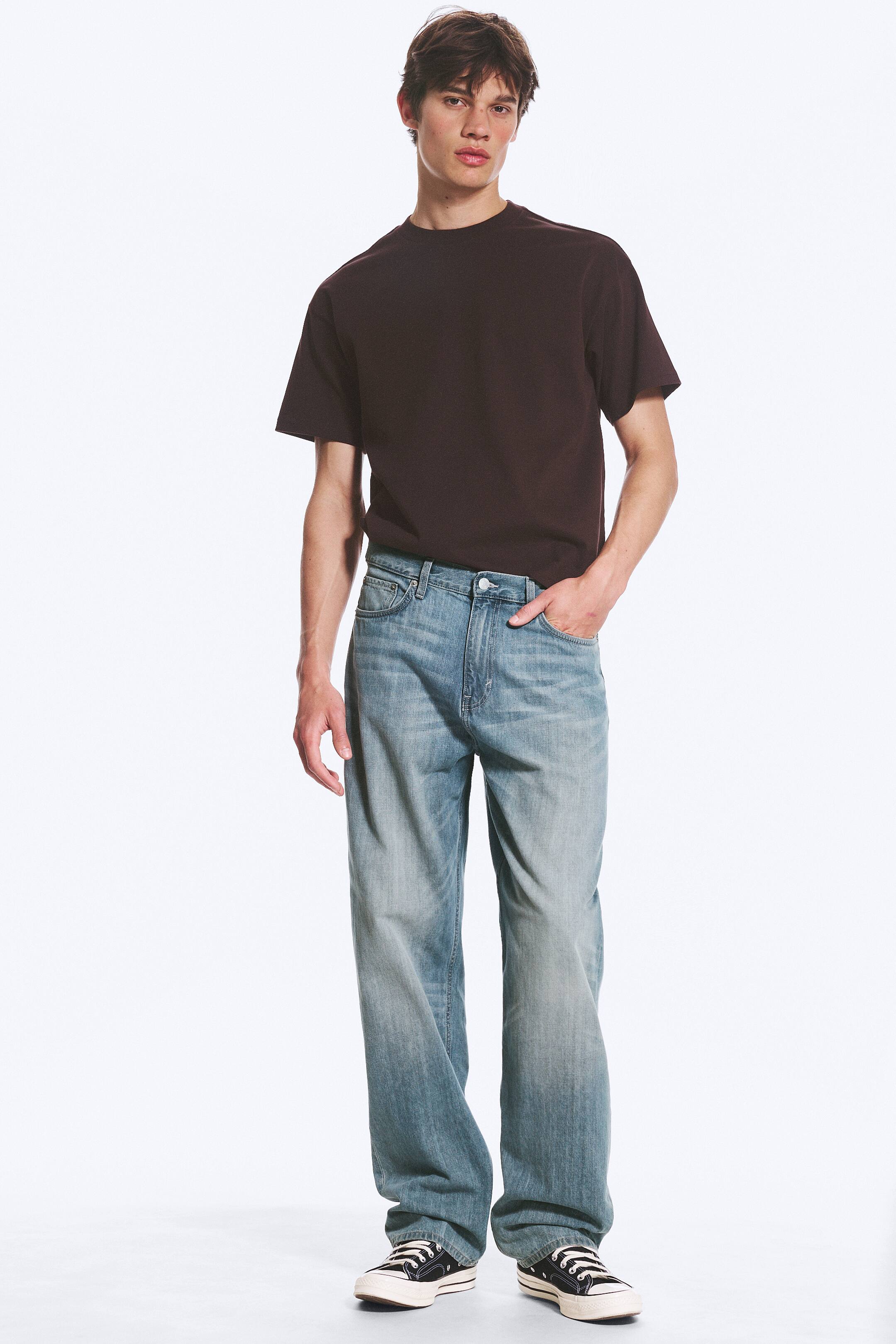 Agrandir l'image: Un t-shirt à col rond marron foncé est porté, rentré dans un jean bleu à jambes larges et délavage clair, avec des poches avant et un effet délavé visible. Des baskets en toile noires sont portées avec le jean, l'ensemble de la tenue étant présenté de face.