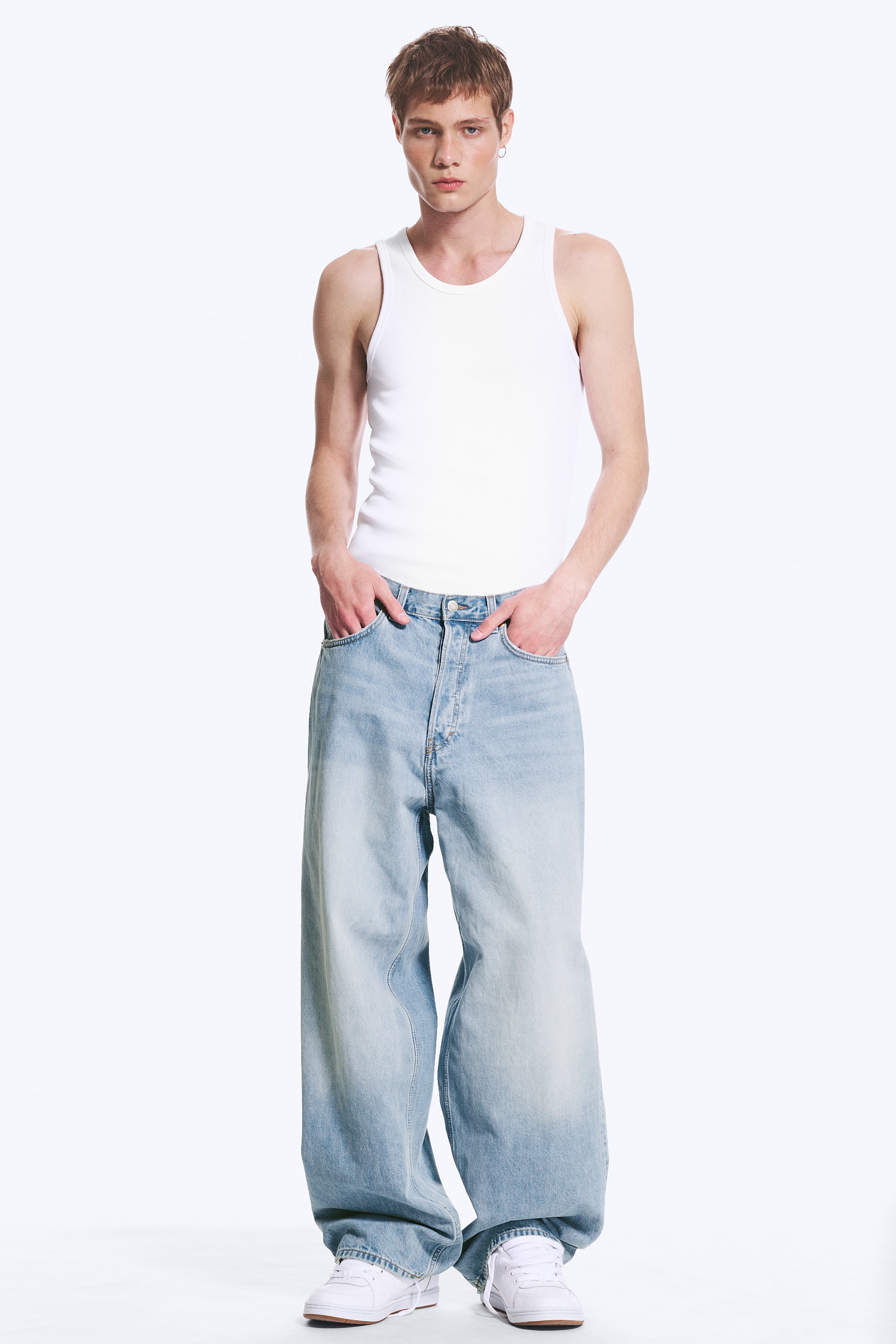 Agrandir l'image: Jean à délavage clair, taille mi-haute, coupe ample et jambe baggy, porté par deux mannequins. Le jean présente une braguette à boutons et des poches avant visibles. Un mannequin est debout, les mains sur les hanches, tandis que l’autre est debout, les mains dans les poches avant du jean.