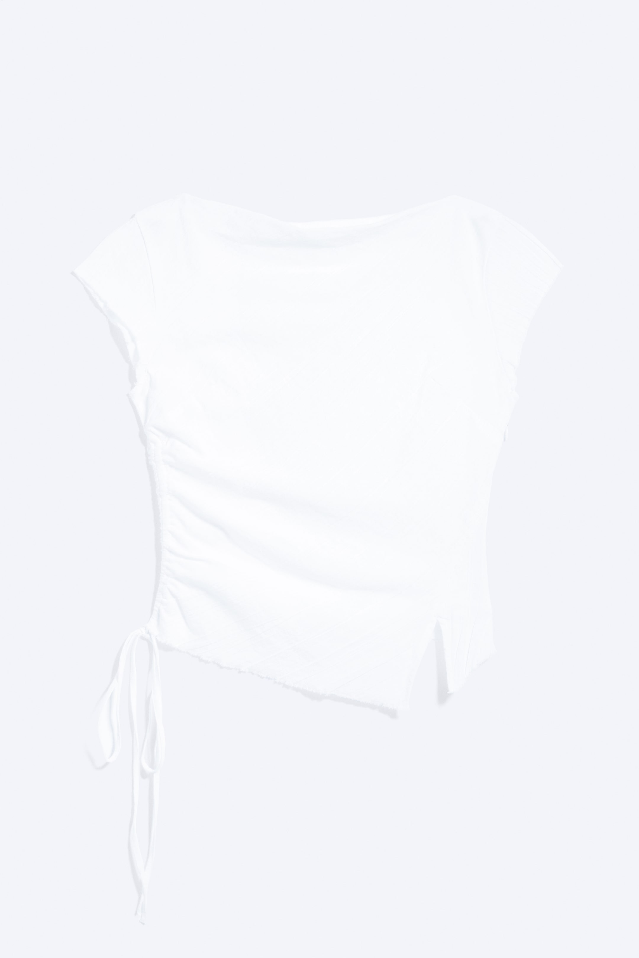 Visualizza immagine più grande: "Un top bianco a maniche corte è mostrato frontalmente, caratterizzato da un ampio scollo e maniche con bordo grezzo. Il lato sinistro presenta una arricciatura con due lacci e l'orlo è asimmetrico."