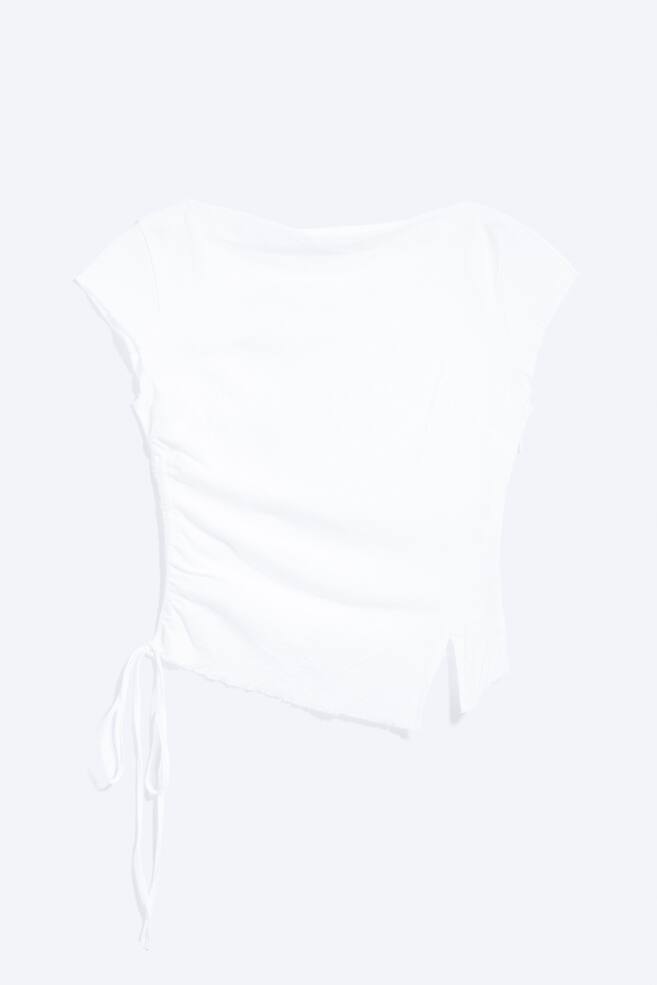 A white short-sleeved top is displayed from the front, featuring a wide neckline and raw edge sleeves. The left side is ruched with two ties, and the hemline is asymmetrical. - 1