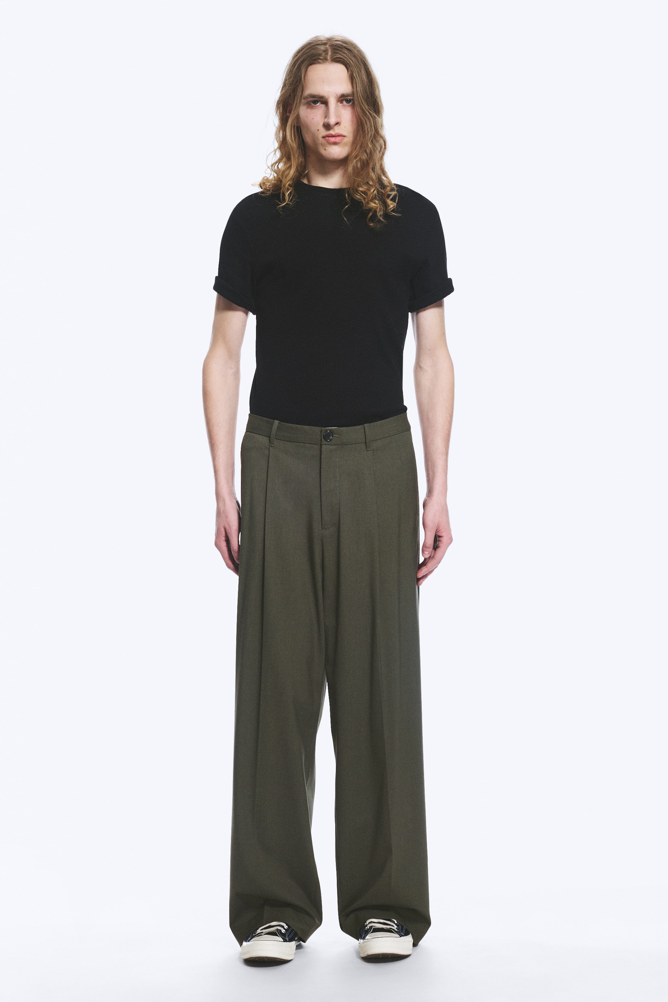Grotere afbeelding bekijken: Een aansluitend zwart T-shirt met korte mouwen en opgerolde boorden wordt gedragen met olijfgroene wijde broek met een geplooide voorkant, een knoopsluiting en een losse, ontspannen pasvorm, allemaal naar voren gericht.