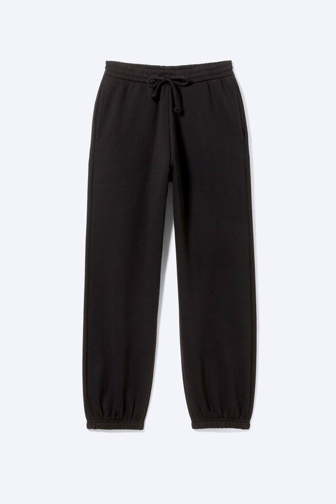 A pair of black joggers is facing front-on. The joggers feature an elasticated waistband with a visible drawcord tied in a knot, side pockets, and ribbed cuffs at the ankles. - 1