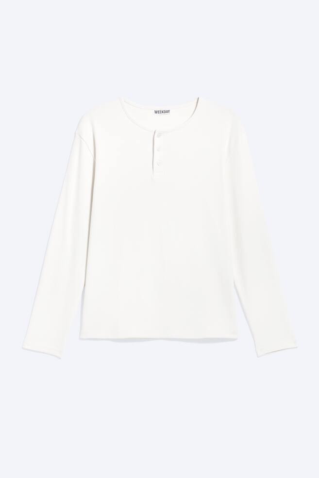 De crèmekleurige top met lange mouwen is aan de voorkant gericht en heeft een ronde halslijn met een Henley-sluiting met drie knopen en lange mouwen. De merknaam "WEEKDAY" is zichtbaar aan de binnenkant van de achterhals, en de zoom onderaan is recht. - 1