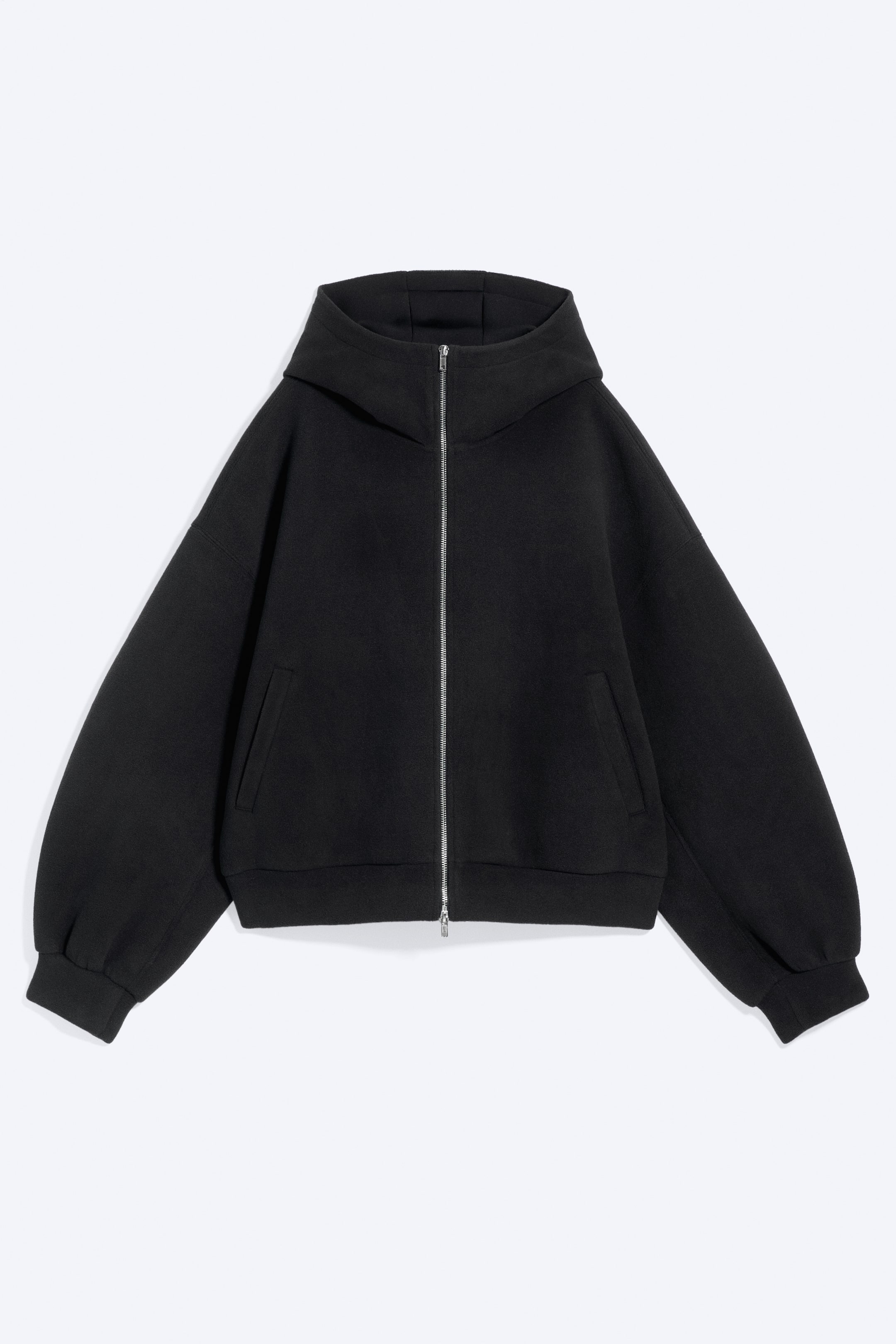 Grotere afbeelding bekijken: Een zwarte hoodie is van voren te zien, met een volledige zilverkleurige ritssluiting en een hoge opstaande kraag die een капuchon vormt. Het model heeft lange, wijde mouwen met elastische boorden, twee paspelzakken vooraan en een elastische zoom.