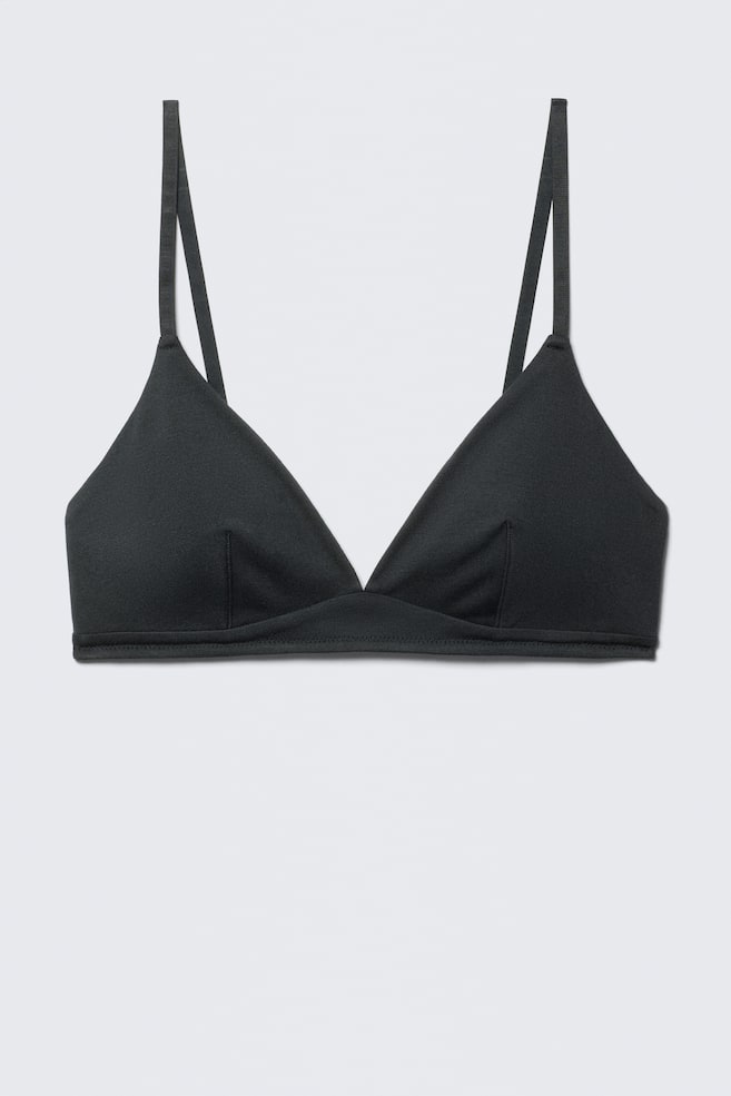 A black bralette is presenting FRONT, featuring triangular cups with vertical seams and thin spaghetti straps. A flat, stitched band is forming the base of the garment. - 1