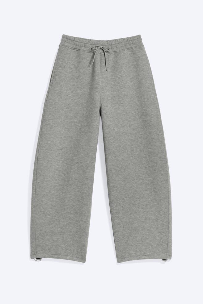 Grey wide-leg sweatpants are lying flat, featuring an elasticated waistband with a tied drawstring and side seam pockets. Small toggles are visible on the inside of the straight hems. - 1