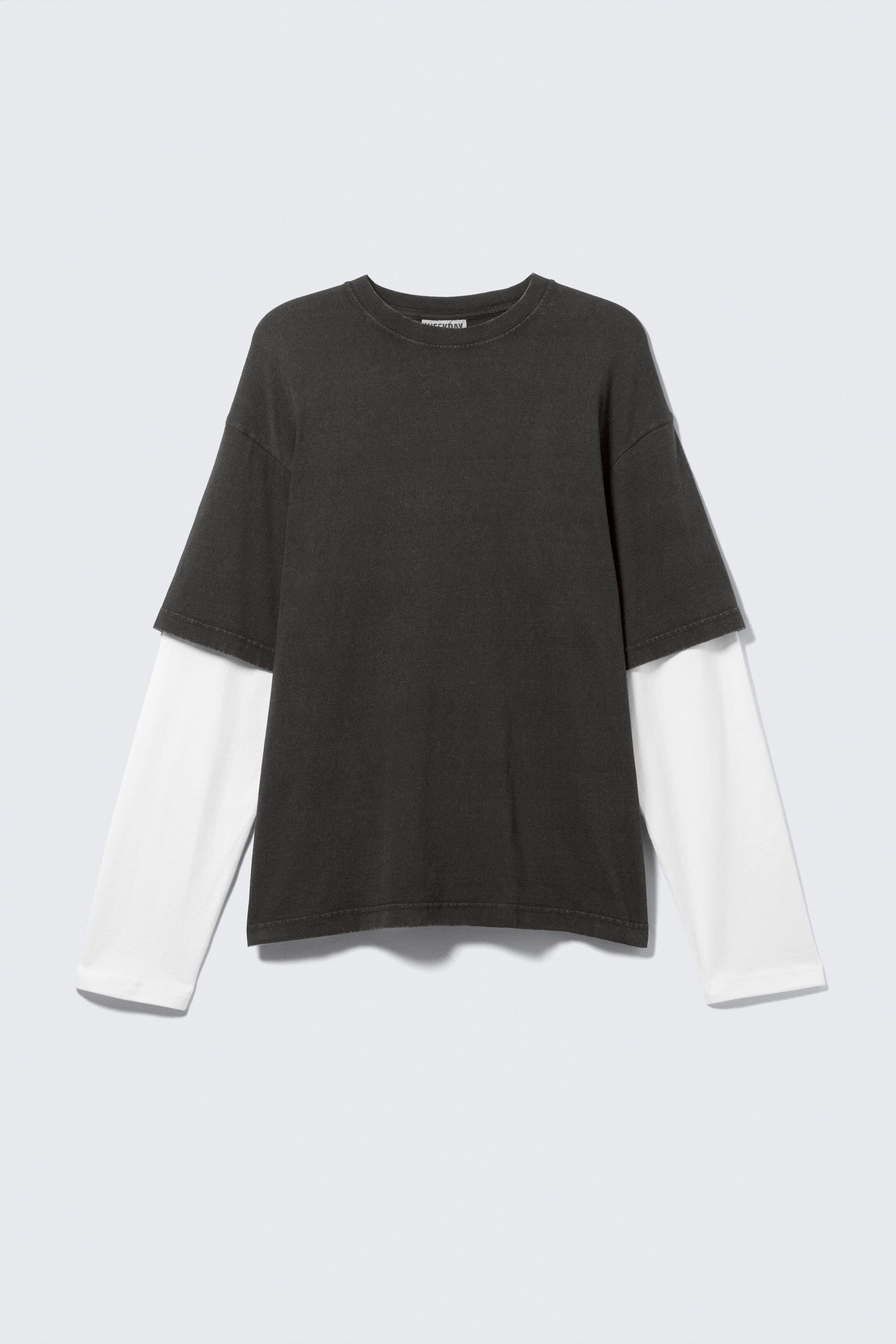 View larger image: A front view of a layered shirt is displayed, featuring a dark charcoal short-sleeve crew neck t-shirt worn over a white long-sleeve t-shirt. The white long sleeves are extending past the short sleeves of the charcoal shirt, with its white hem visible below the charcoal shirt's hem.