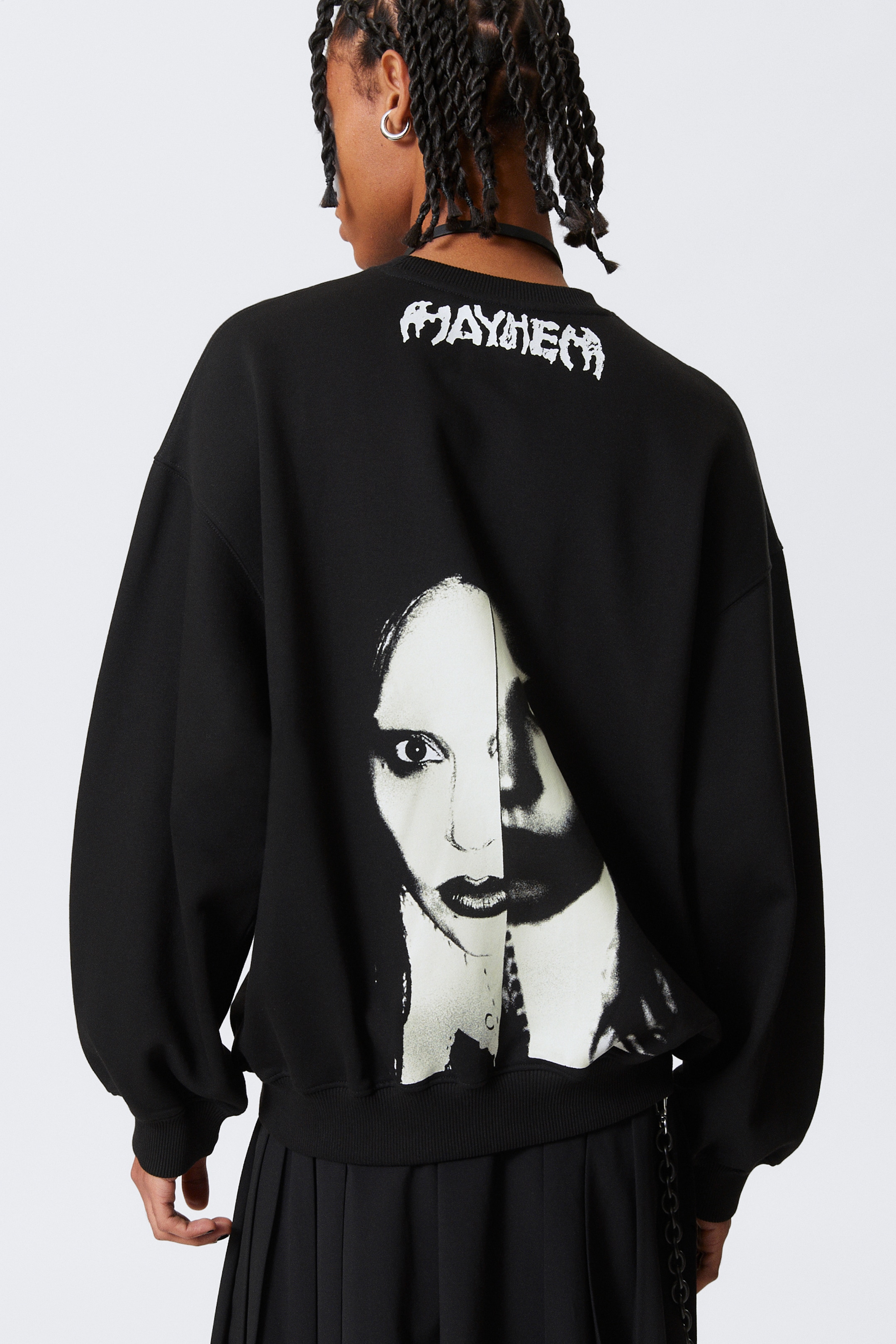 Agrandir l'image: Un sweat-shirt noir surdimensionné est présenté de dos, avec le texte "MAYHEM" en police blanche usée sur le haut du dos. En dessous du texte, un grand graphique noir et blanc à fort contraste représentant un visage fendu est visible, et le sweat-shirt présente des poignets côtelés et un ourlet côtelé.