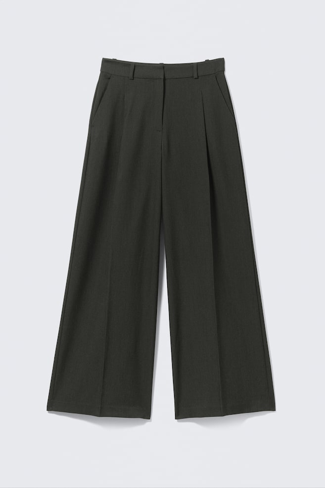 A pair of dark charcoal-toned, high-waisted suiting trousers is presented FRONT, featuring a loose fit and wide leg. They showcase sharp front pleats, slanted side pockets, belt loops, and a hook-and-eye zip fly, all crafted from structured twill. - 1