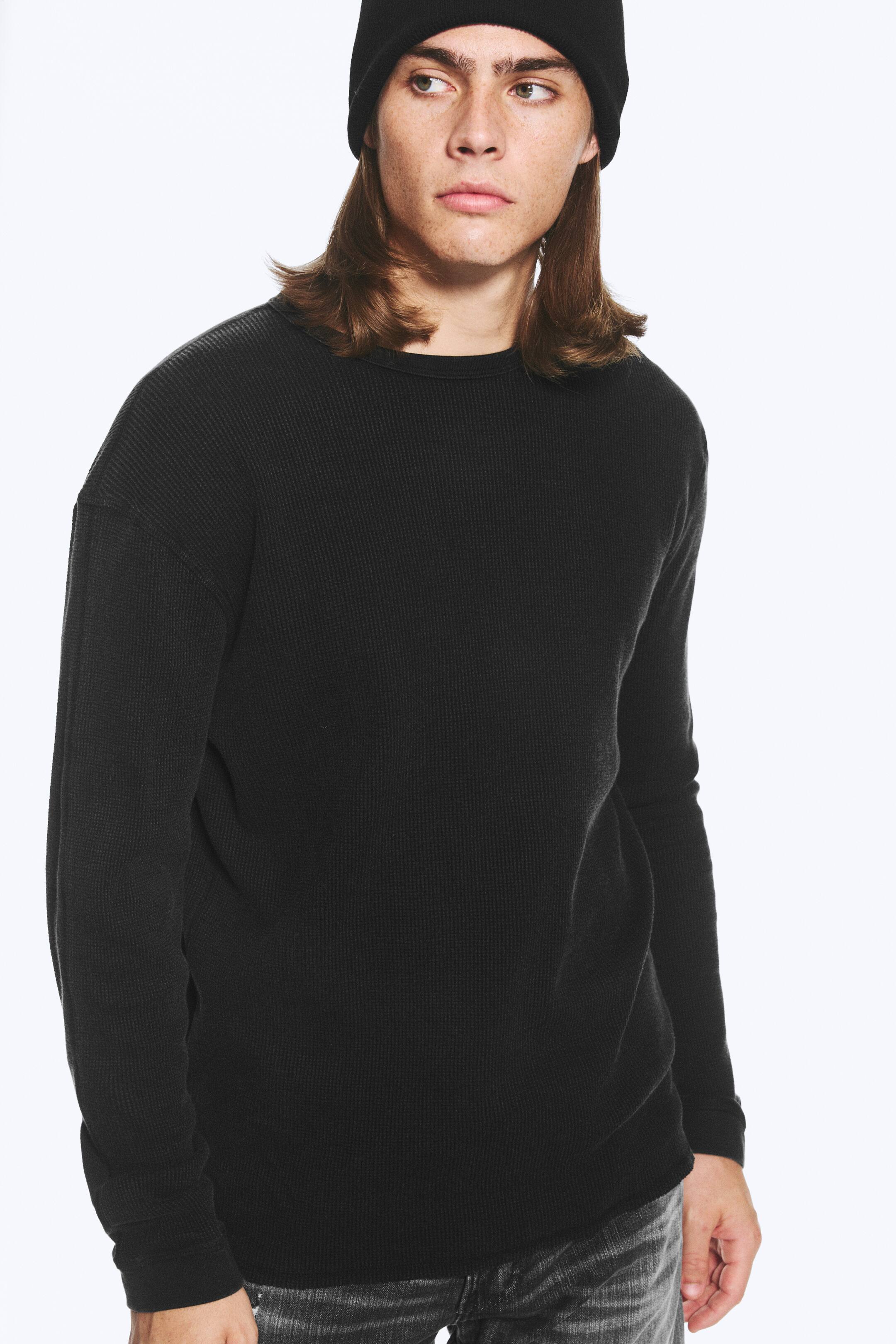 Grösseres Bild ansehen: Ein schwarzes, locker geschnittenes Langarm-T-Shirt aus Waffelstrick mit Rundhalsausschnitt wird vom Model getragen.