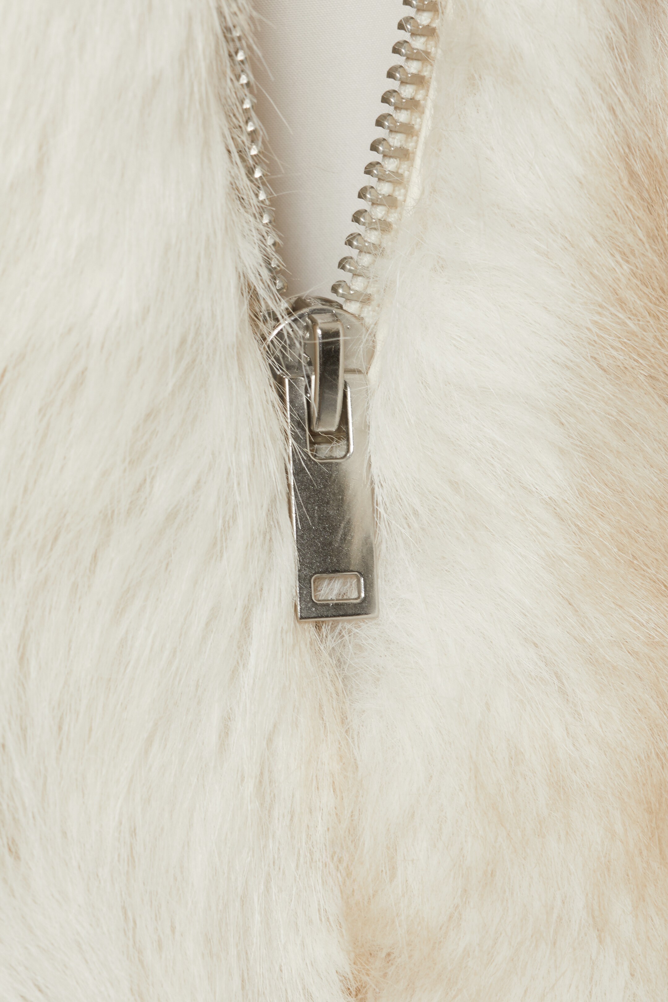 View larger image: A white faux fur garment is featuring a partially visible silver-toned metal zipper, with its pull and teeth clearly showing.
