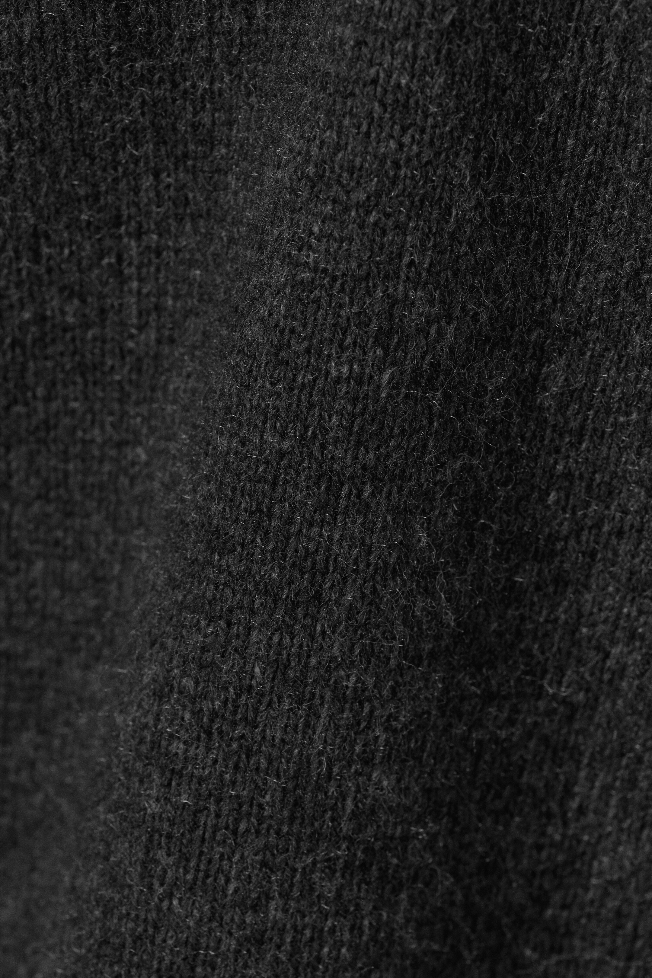 View larger image: A dark grey knitted fabric is showing its textured surface in a close-up view. The fabric is displaying distinct vertical stitches and a slightly fuzzy finish.