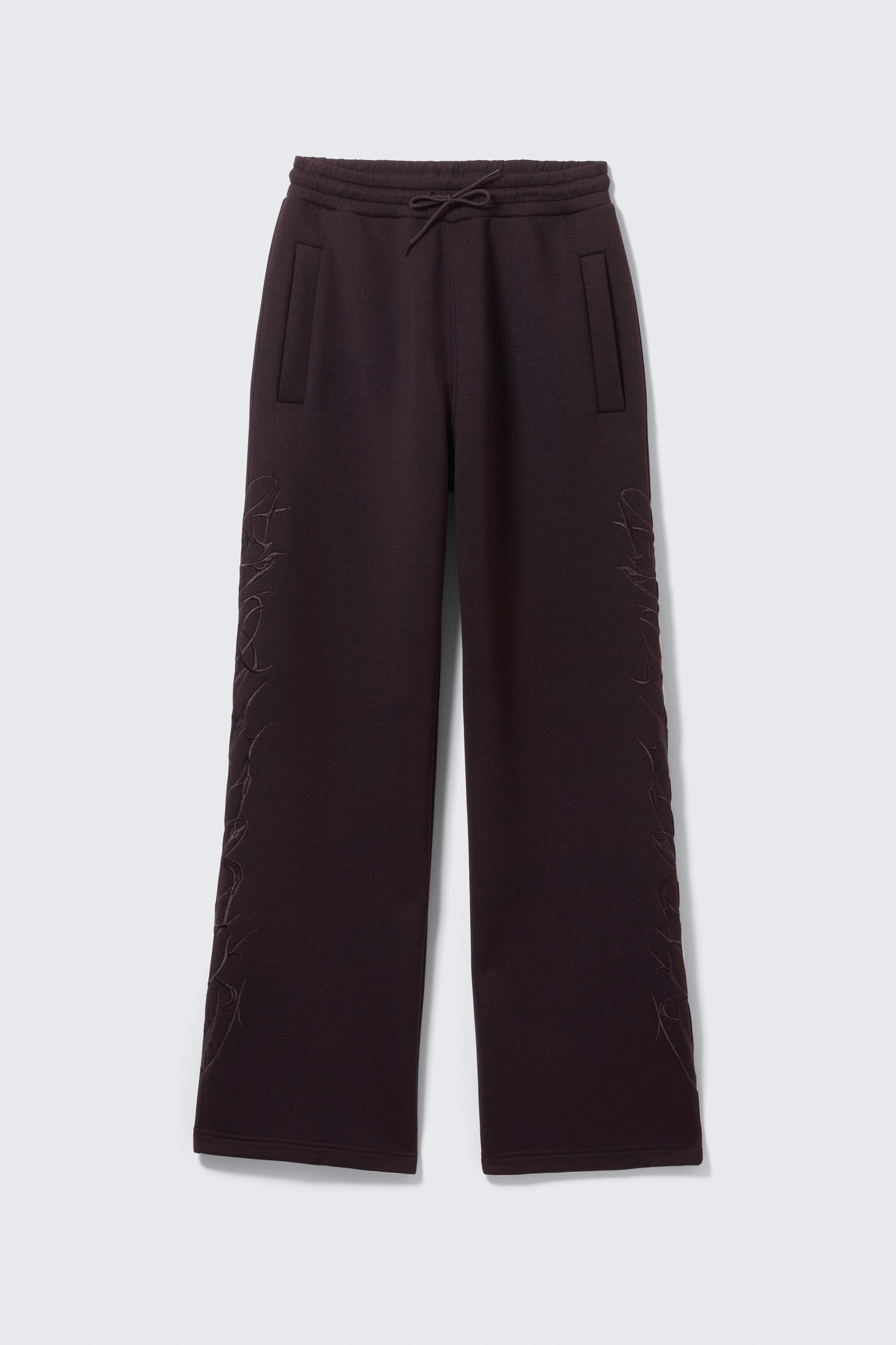 Agrandir l'image: Vue de face d'un pantalon de jogging à jambes larges brun foncé, doté d'une taille élastiquée avec un cordon de serrage, de deux poches avant verticales et d'une broderie abstraite subtile ton sur ton longeant la couture extérieure de chaque jambe.