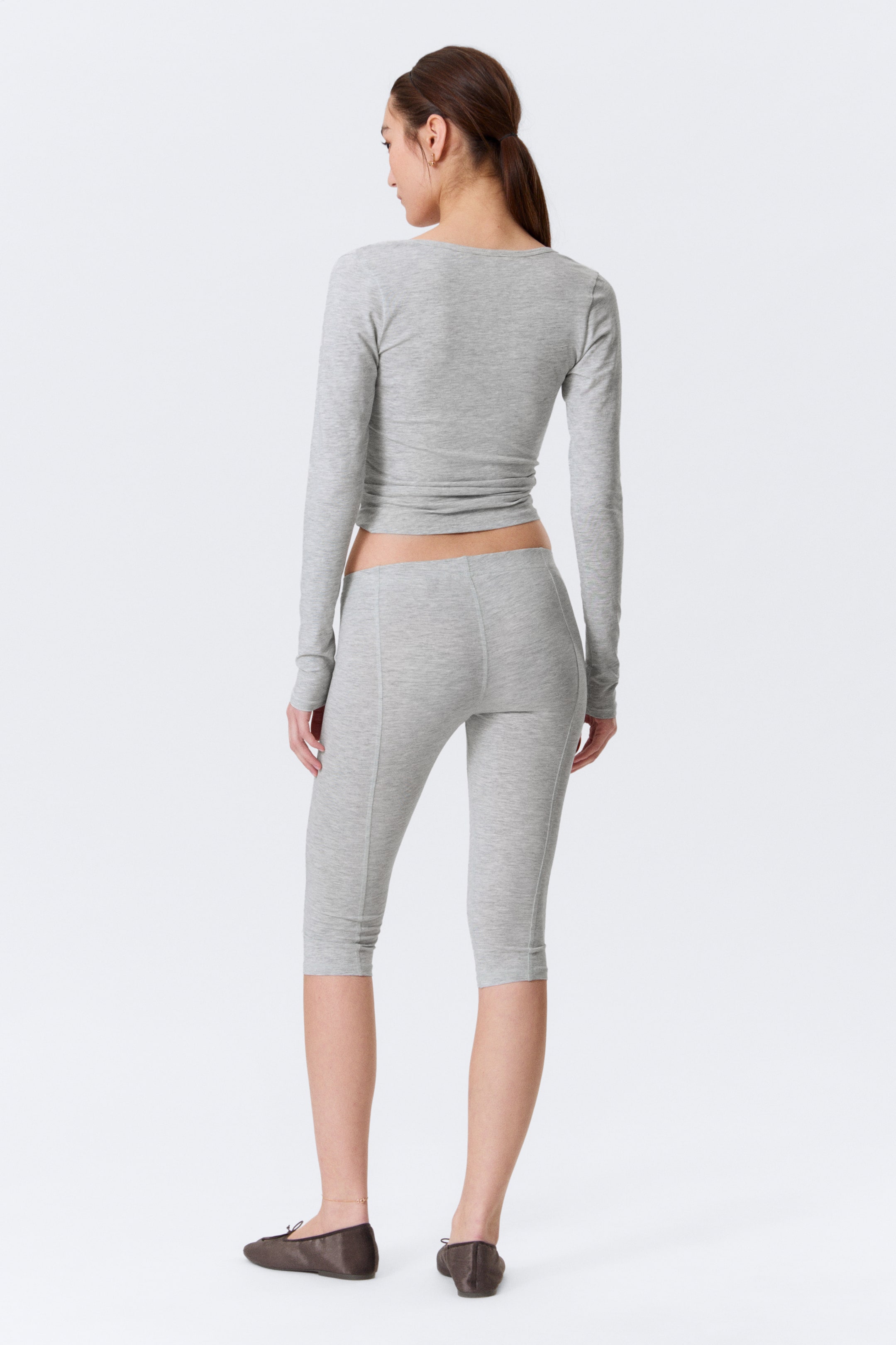 Agrandir l'image: Un haut à manches longues gris clair et des leggings capri assortis sont présentés de dos. Le haut présente un large col et une coupe courte, tandis que les leggings ajustés affichent des détails de coutures verticales courant le long de l'arrière de chaque jambe.