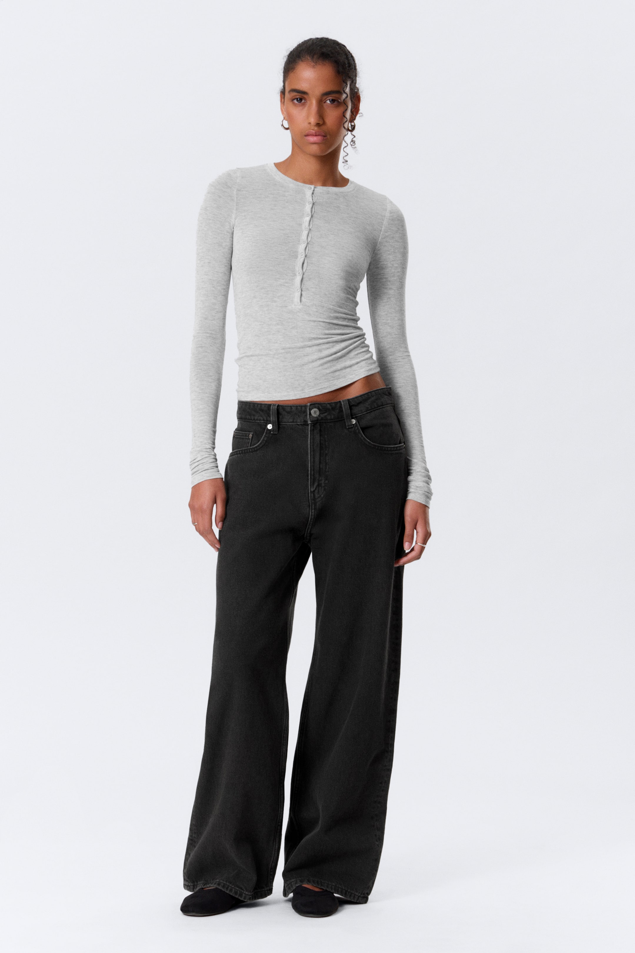 Visualizza immagine più grande: Un top Henley a maniche lunghe grigio chiaro presenta una vestibilità aderente, uno scollo tondo e un'abbottonatura parziale sul davanti, indossato con jeans a gamba larga grigio scuro che si posizionano alti in vita.