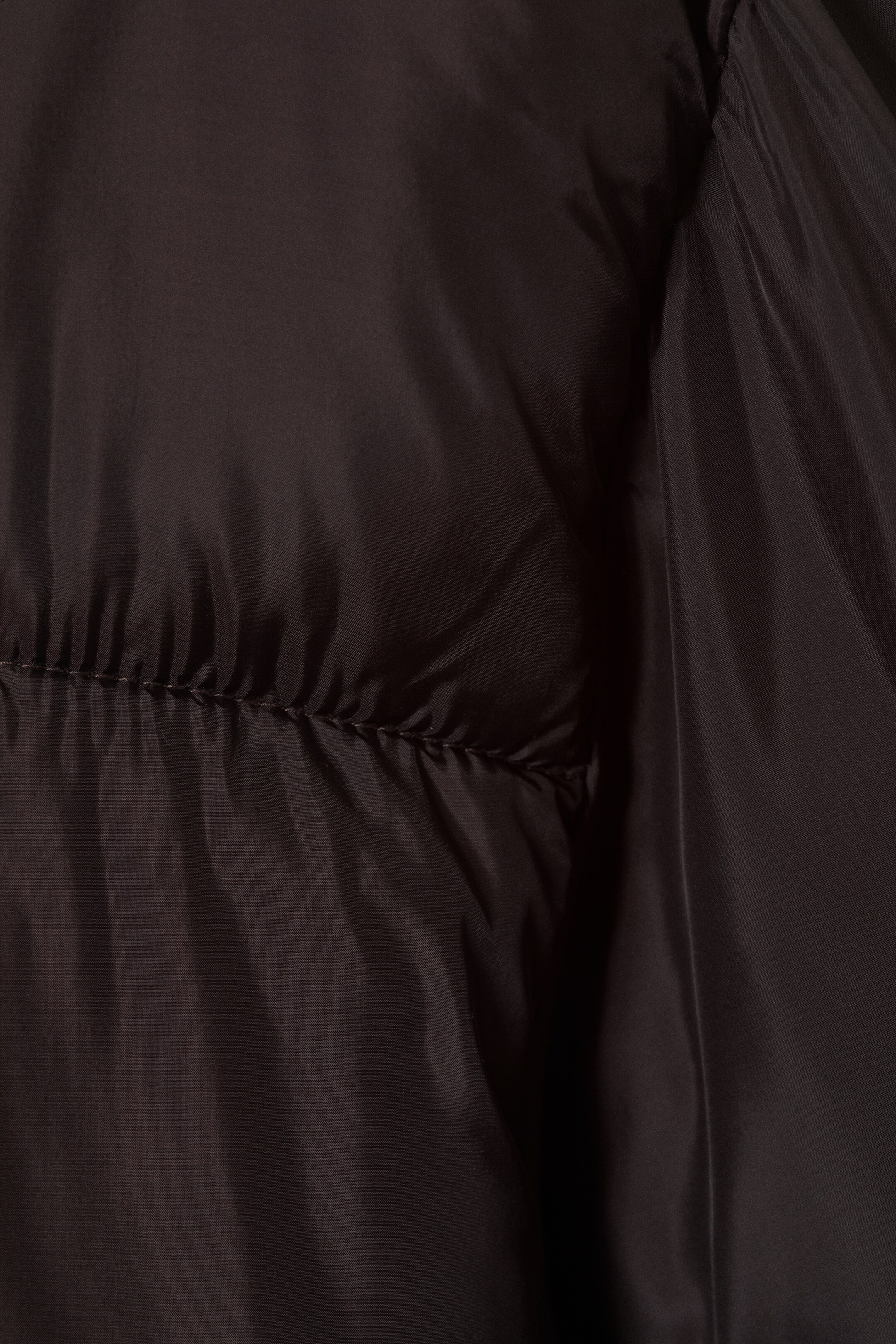 View larger image: A dark, possibly black, padded fabric is featuring a horizontal seam with visible stitching. The fabric is softly gathering around the seam, creating a puffed, quilted texture.