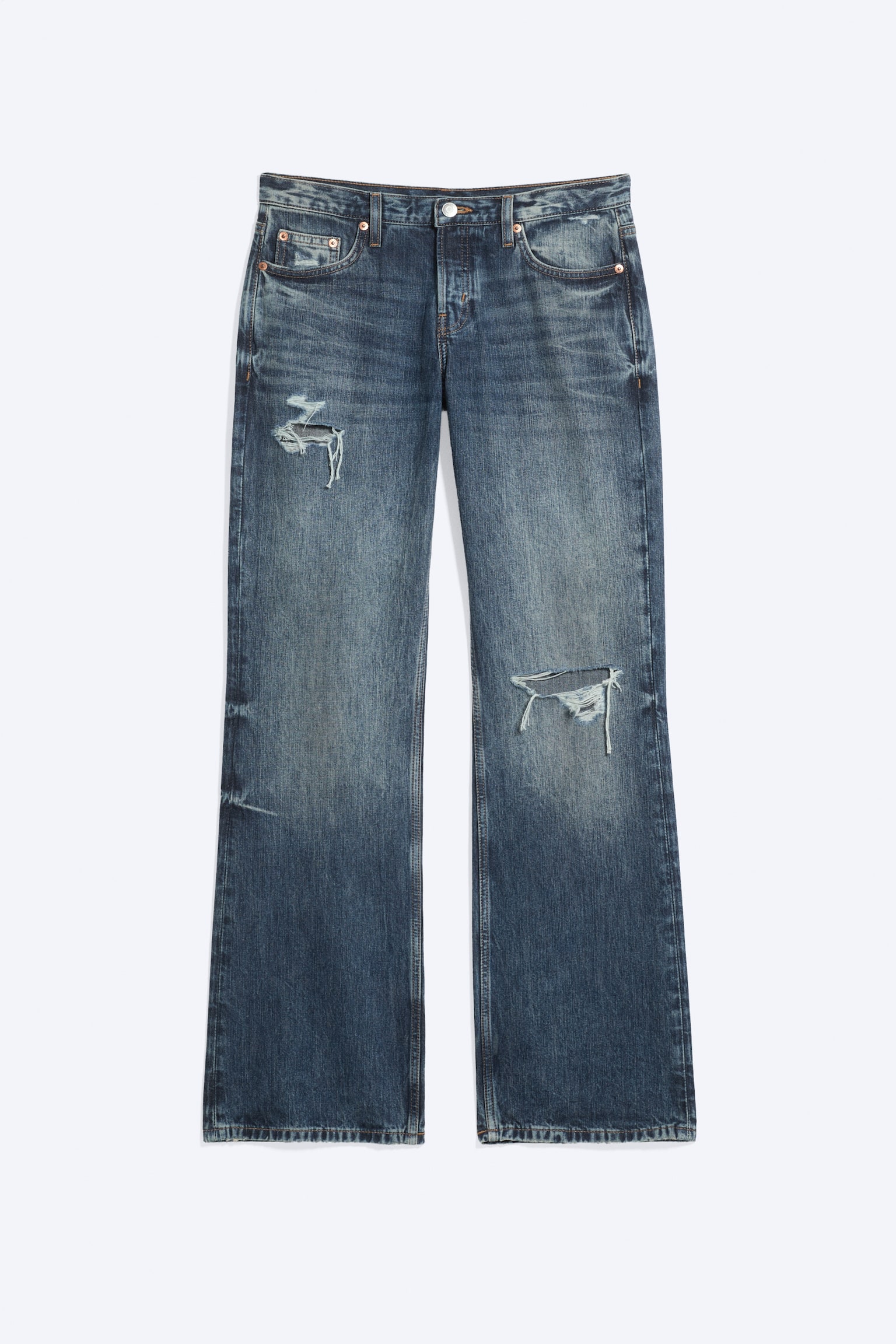 Jeans bootcut de tiro bajo y corte relajado en un lavado azul desteÃ±ido, vistos de frente, con diseÃ±o clÃ¡sico de cinco bolsillos, efecto whiskering y rotos desgastados en la parte superior del muslo derecho y en la rodilla izquierda.