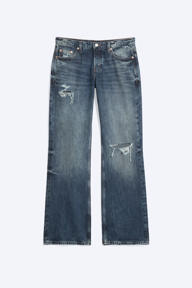 Jeans med låg midja och avslappnad bootcut-passform i en blekt blå tvätt visas framifrån, med klassisk femficksdesign, whiskering och slitna revor på högra övre låret och vänster knä. - 1