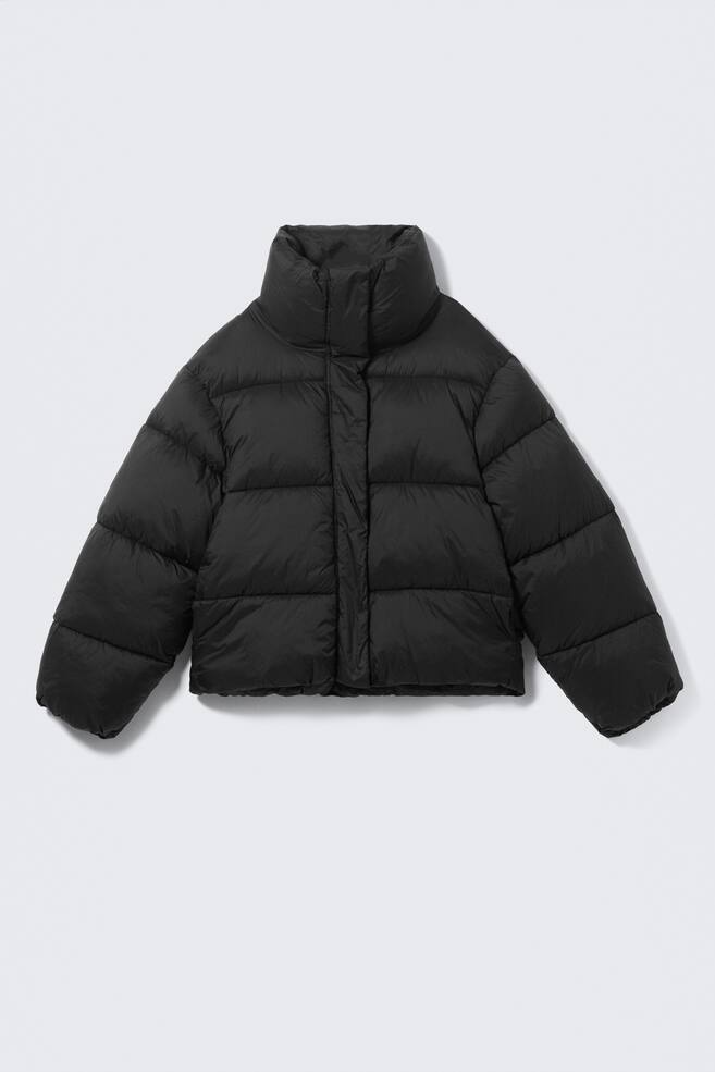 A black cropped puffer jacket is being shown from a front view. It is featuring a high stand collar, horizontal quilting, and a hidden front closure. The jacket is designed with long, voluminous sleeves ending in gathered cuffs and a cinched hem, creating a boxy silhouette. - 1