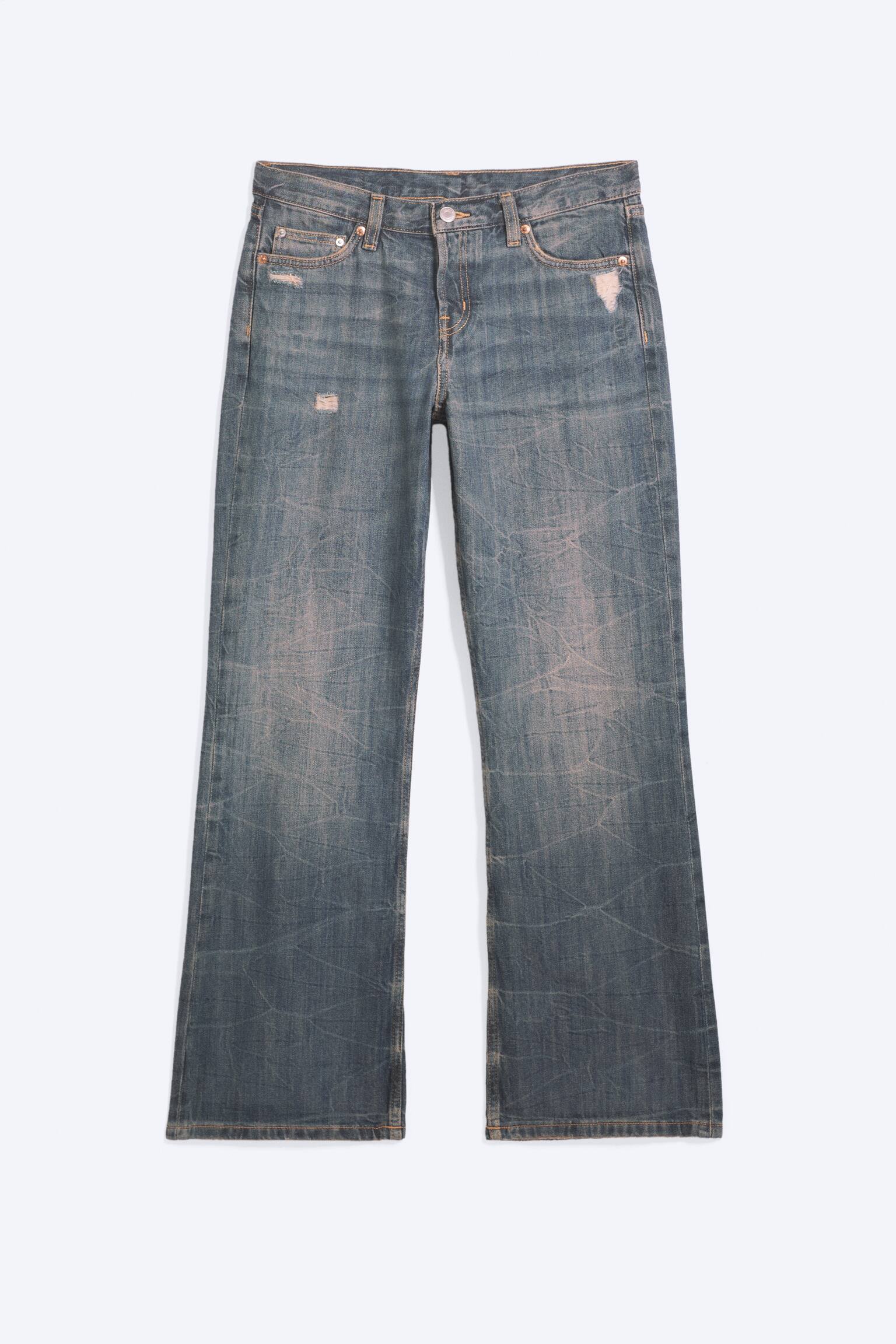 Et par lavtaljede jeans med afslappet pasform og bootcut i en falmet blå vask vises forfra, med et tekstureret krølleeffektmønster over hele stoffet og små slidte detaljer nær lommerne. Jeansene har et klassisk femlommedesign med let svajede ben. - 1