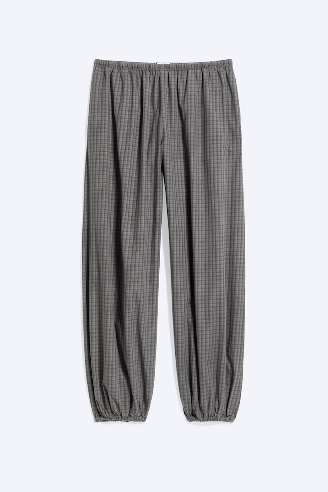 Eine graue Ballonhose mit Karomuster hängt in einer Frontalansicht und zeigt einen gerafften elastischen Bund sowie weite, voluminöse Beine, die in elastische Bündchen auslaufen. - 1