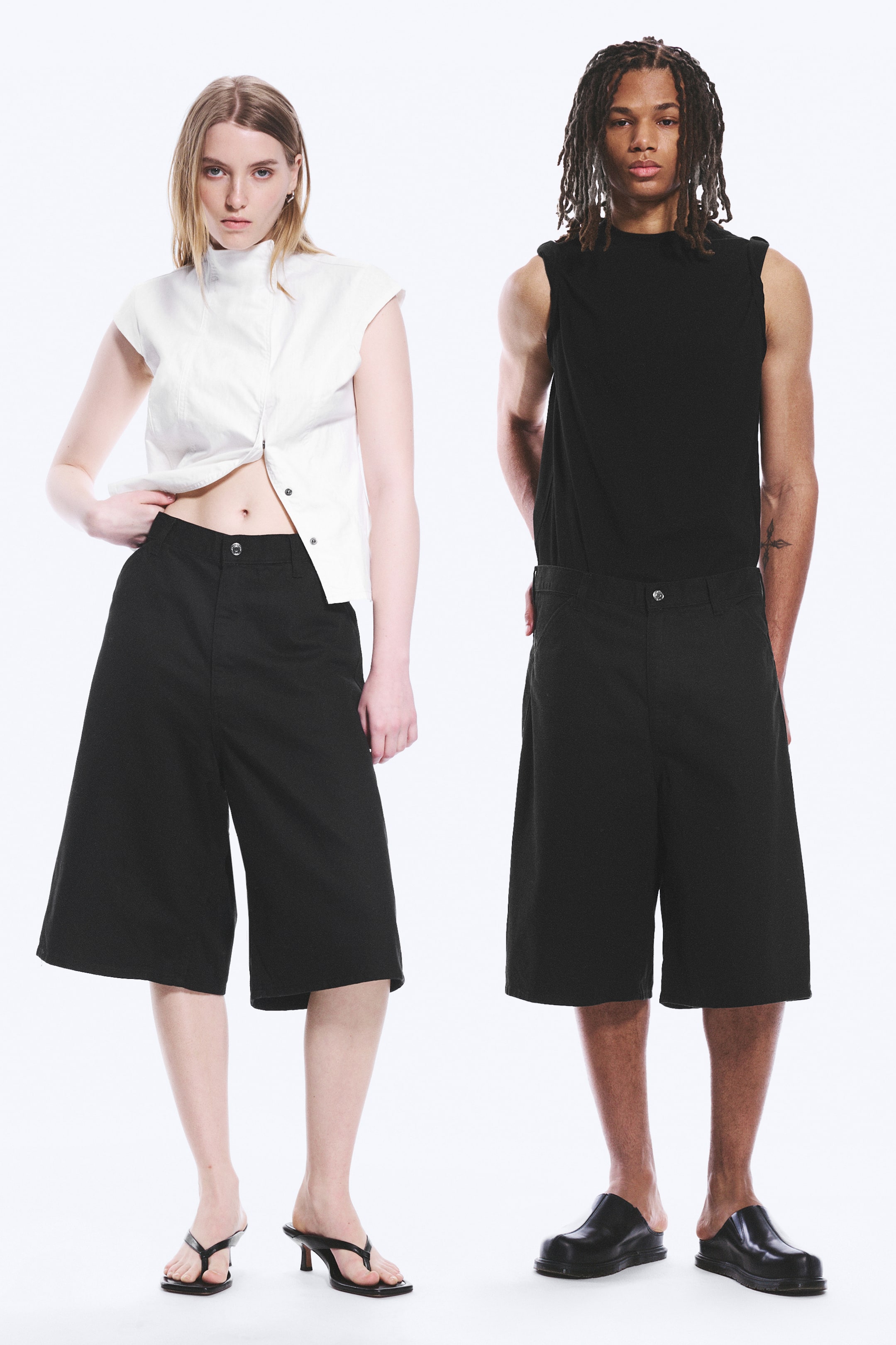 Grotere afbeelding bekijken: Zwarte wijde shorts reiken net onder de knie en hebben een gestructureerde, losse pasvorm met een zichtbare knoopsluiting aan de tailleband. Ze zijn voorzien van heupzakken aan beide zijden.