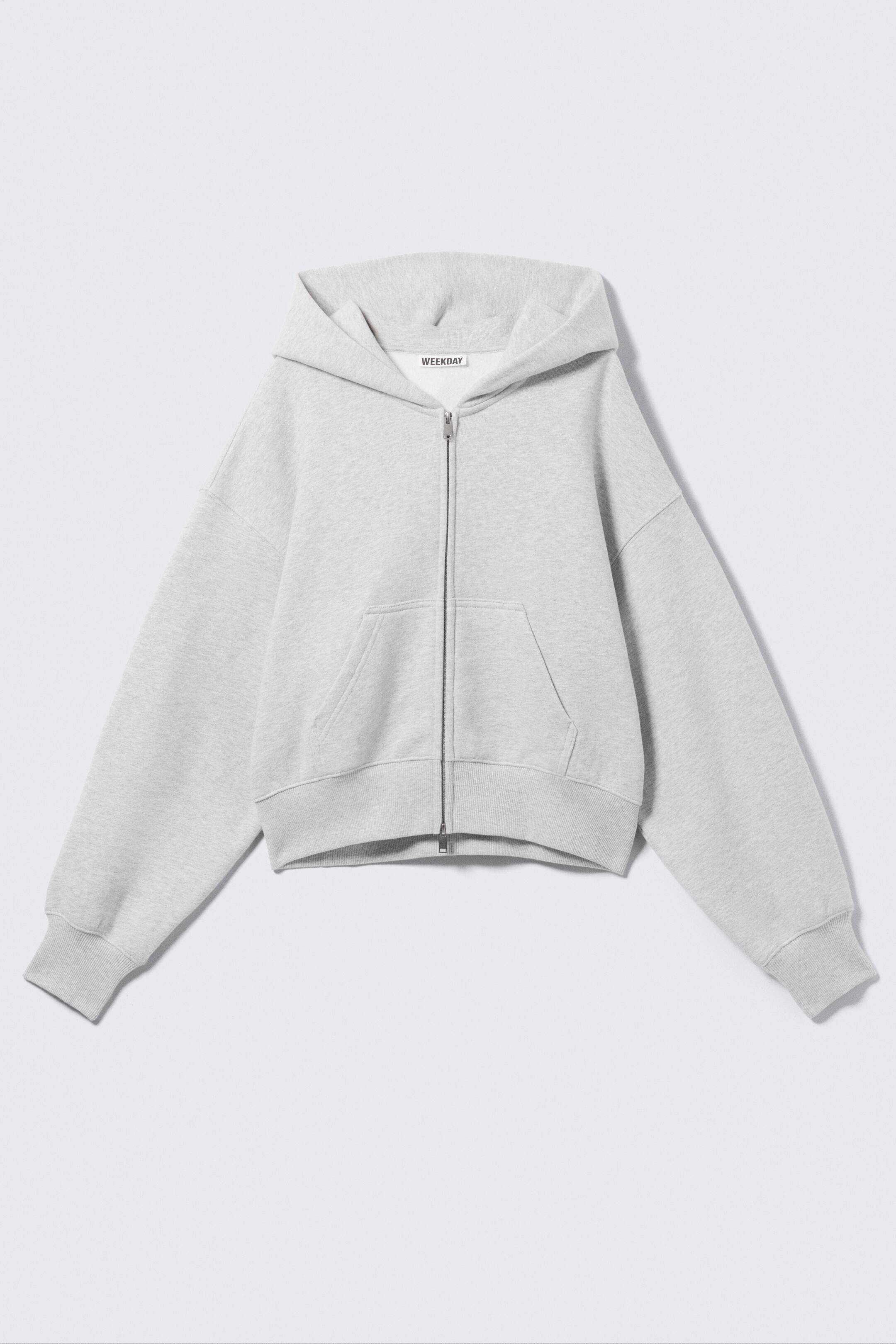 View larger image: A light grey zip-up hoodie is displayed from the front, crafted from soft cotton with a boxy silhouette and a cropped length. It features a relaxed hood, a central front zip, a kangaroo pocket, and ribbed cuffs and hem.