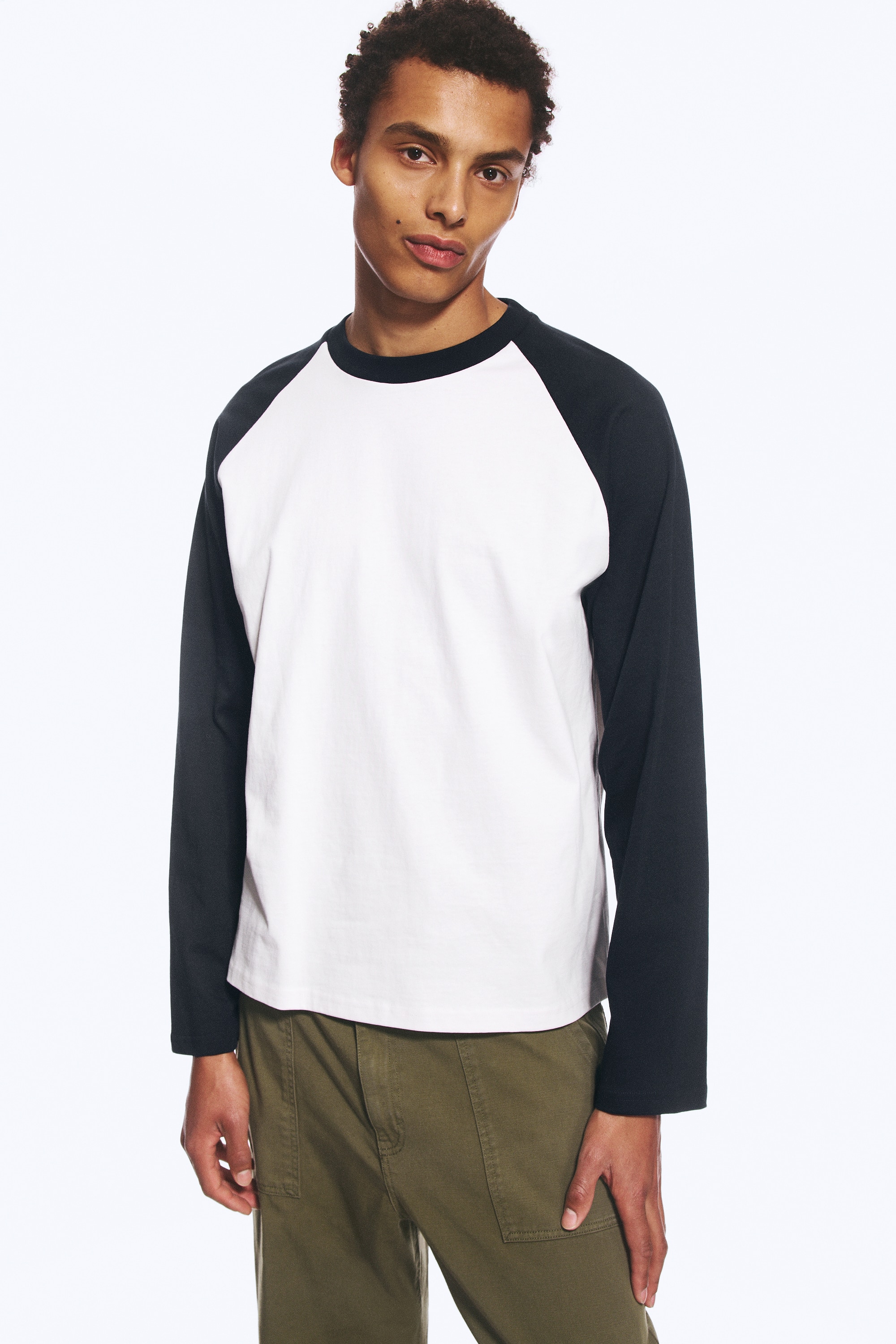 Una T-shirt a maniche lunghe dalla vestibilitÃ  ampia e squadrata Ã¨ ripresa frontalmente, mettendo in risalto un corpo in jersey di cotone bianco con maniche raglan a contrasto in blu navy scuro. Il capo presenta un girocollo coordinato in blu navy scuro e un orlo dritto e pulito.