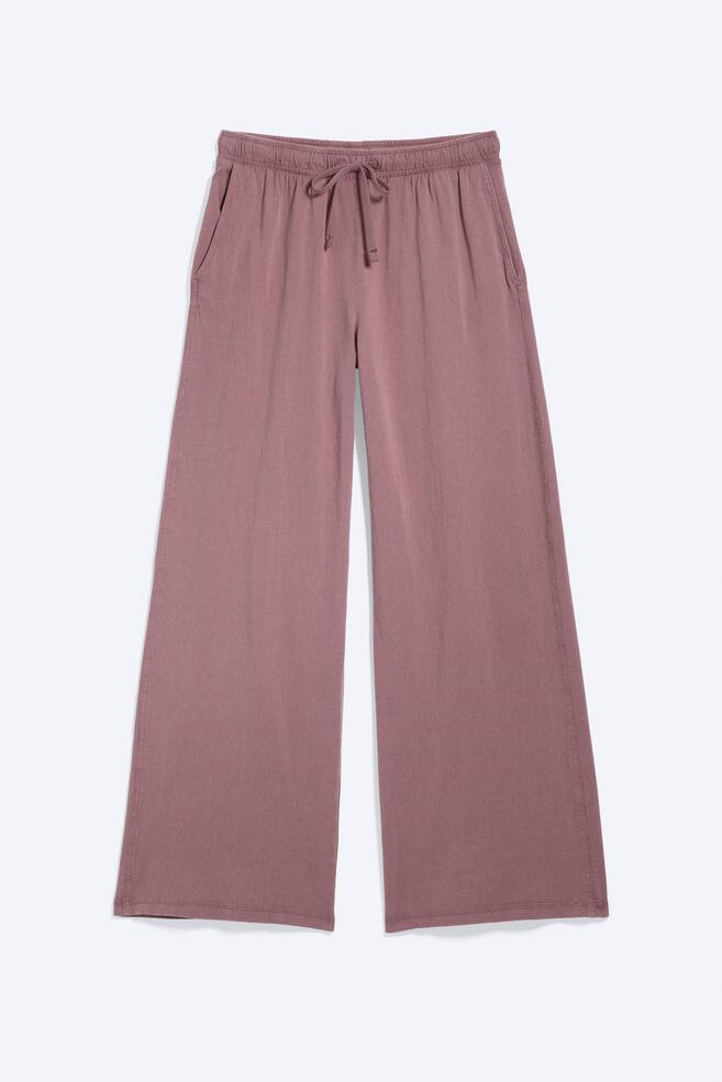 Mauve wide-leg trousers are showcased from the front, featuring an elasticated drawstring waistband with a tied bow and visible side seam pockets. The trousers display a soft, relaxed fabric and a neat hem. - 1