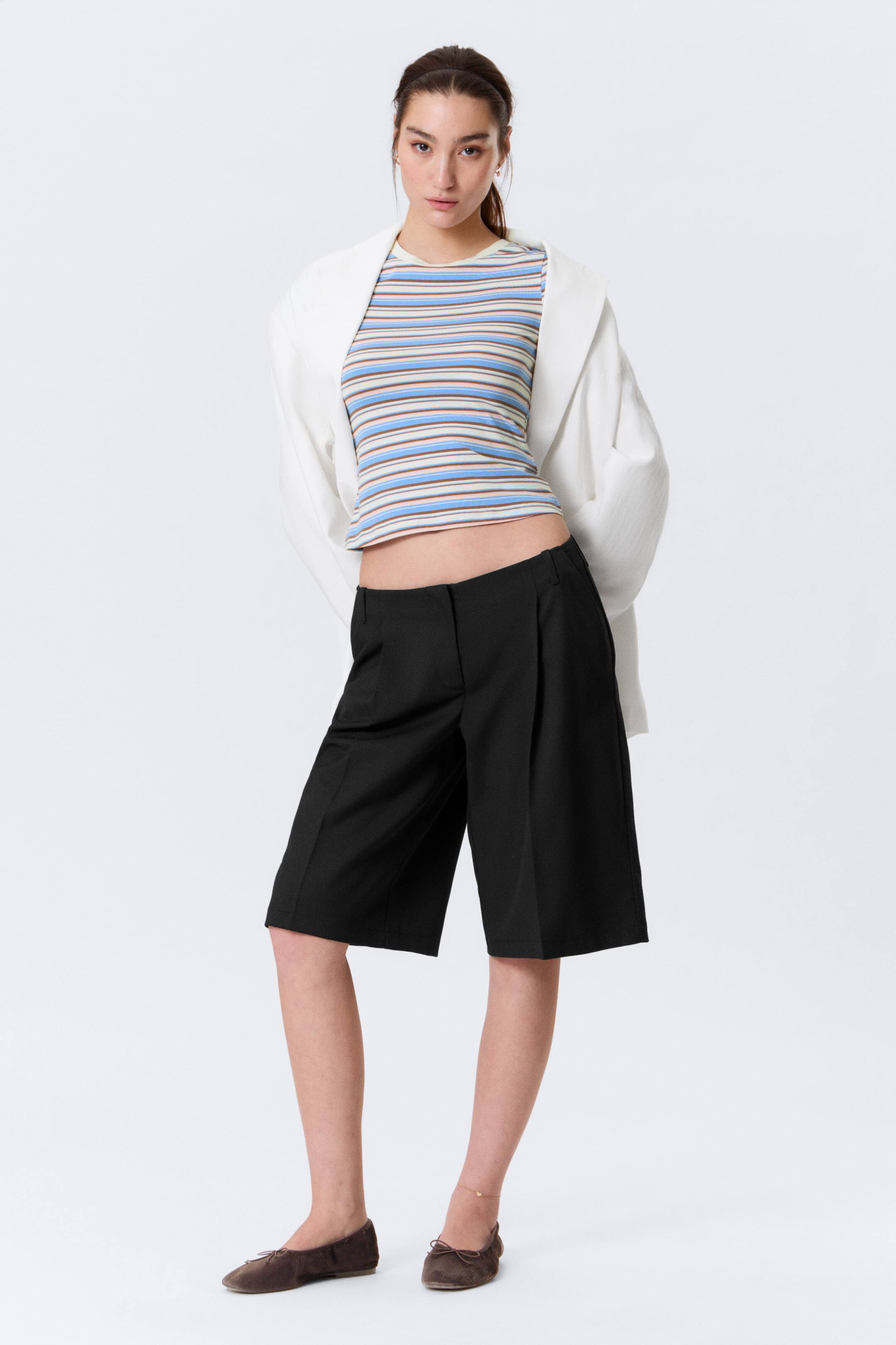 Visa större bild: Svarta knälånga shorts med en bred siluett och framtill veck, vinklade något åt vänster för att framhäva deras struktur.