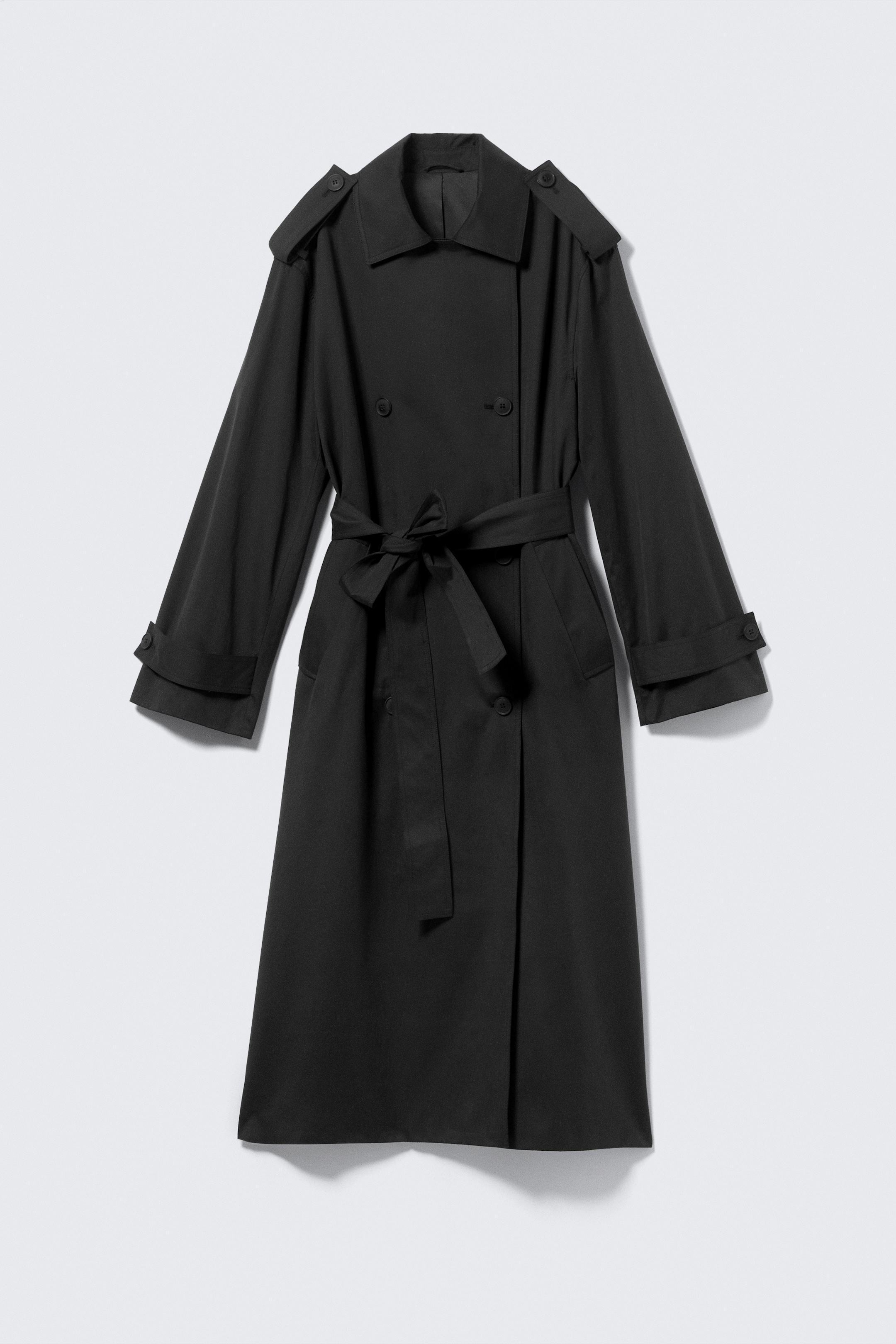 Visualizza immagine più grande: Un trench coat nero doppiopetto è mostrato frontalmente, con una vestibilità oversize e dettagli classici. Presenta un ampio colletto, spalline con bottoni sulle spalle, una pattina antipioggia e tasche a filetto inclinate. Una cintura staccabile è annodata in vita sul davanti, e cinturini regolabili con bottoni sono visibili ai polsini.