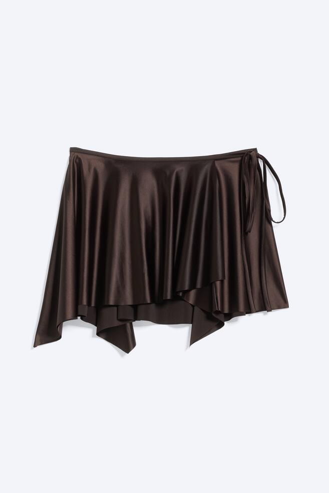 Ein dunkelbrauner Satin-Wickelrock mit einem glänzenden Finish und einem asymmetrischen, drapierten Saum. Er wird durch dünne Bänder auf der rechten Seite gesichert. - 1