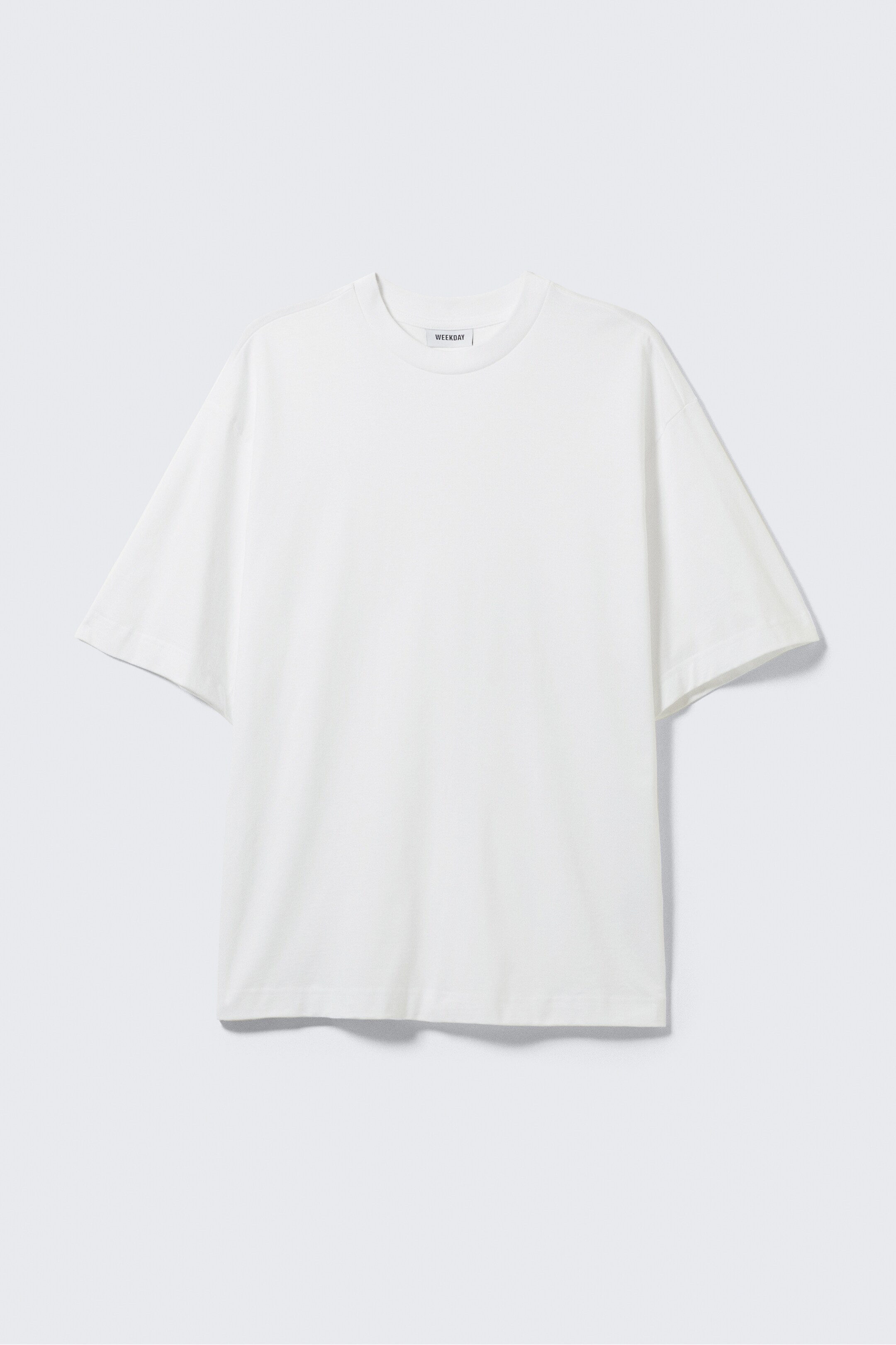 Agrandir l'image: Un t-shirt blanc est orienté vers l'avant, avec un col rond et des manches courtes et larges. Il présente une coupe décontractée en tissu lisse, avec une étiquette de marque 'WEEKDAY' visible à l'intérieur du col.
