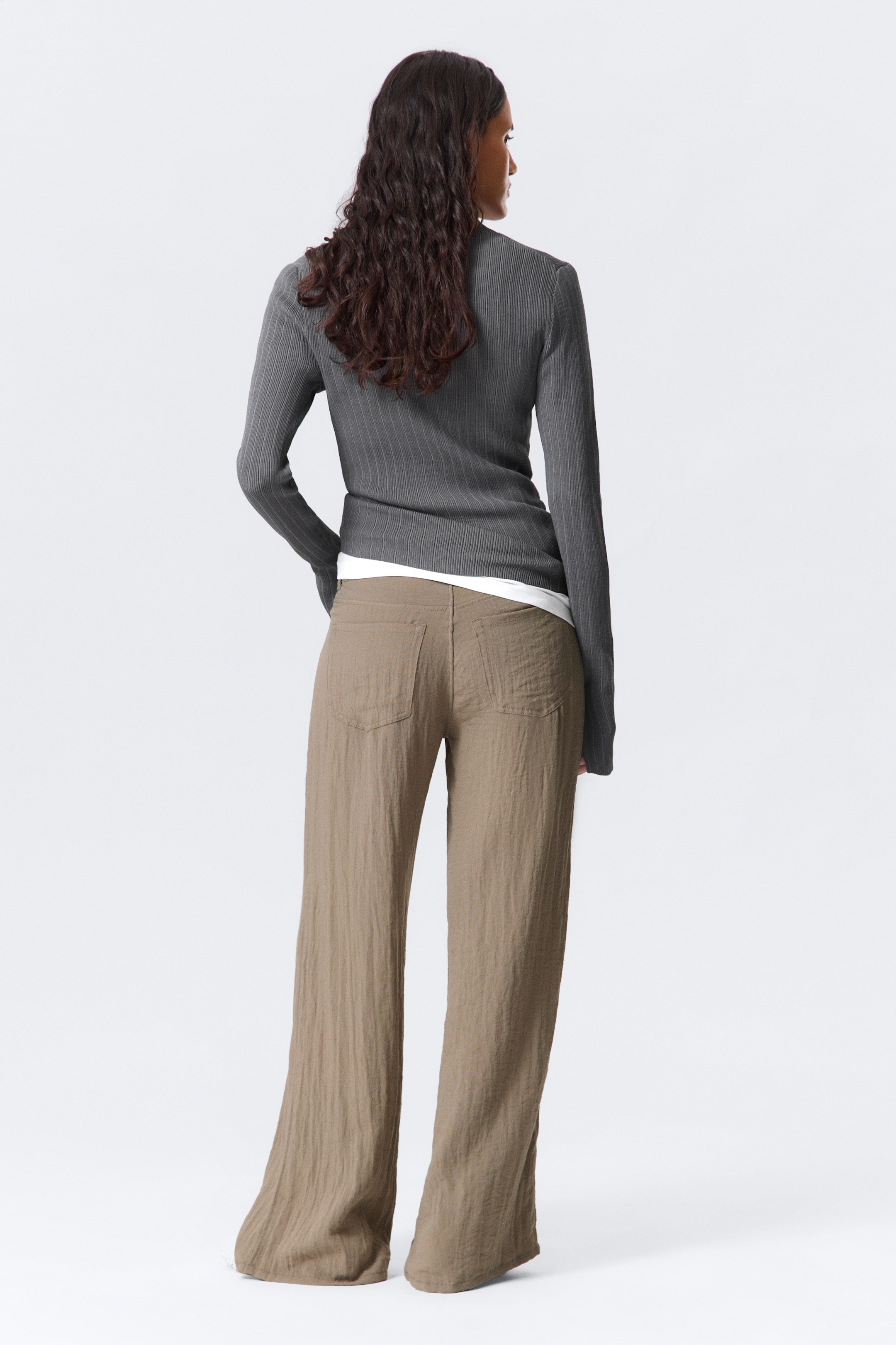 View larger image: A grey ribbed long-sleeve top and brown wide-leg pants are being shown from the back. The fitted ribbed top is layered over a white garment, while the loose, wide-leg pants feature a visible crinkled texture and back pockets.
