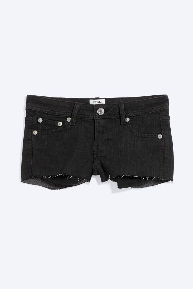 Black denim very short, low-rise, slim-fit shorts are shown from the front, featuring a button fastening with a zip fly, two front pockets with metal rivets, a coin pocket, and a raw, frayed hem. A 'MONKI' label is visible on the top centre waistband. - 1