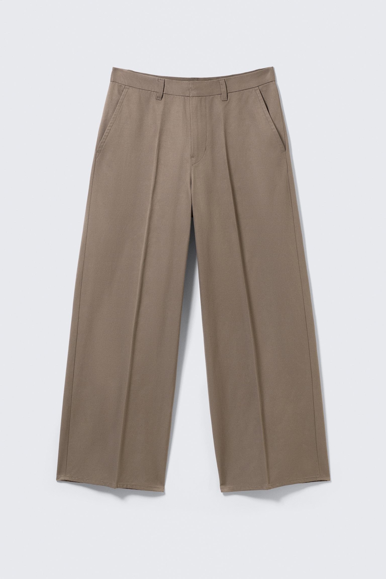 Ein Paar locker sitzende, hellbraune Chino-Hosen wird von VORNE gezeigt. Die Hosen bestehen aus strukturiertem Twill und verfügen über Gürtelschlaufen, einen Reißverschluss und schräge Seitentaschen. Bügelfalten verlaufen entlang der Vorderseite jedes weiten Beins.