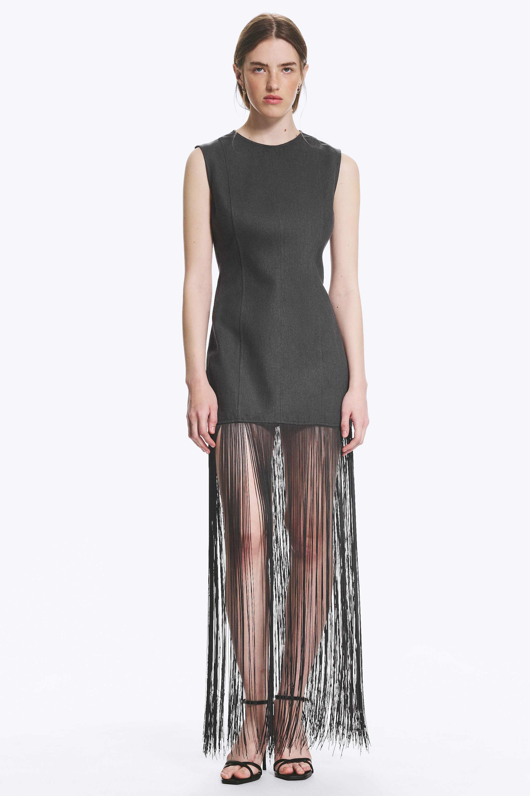 Agrandir l'image: Une mini-robe sans manches gris foncé, présentée de face, est dotée d'un col rond et de coutures à l'avant, avec une superposition de longues franges noires s'étendant de l'ourlet de la mini-robe jusqu'aux chevilles.